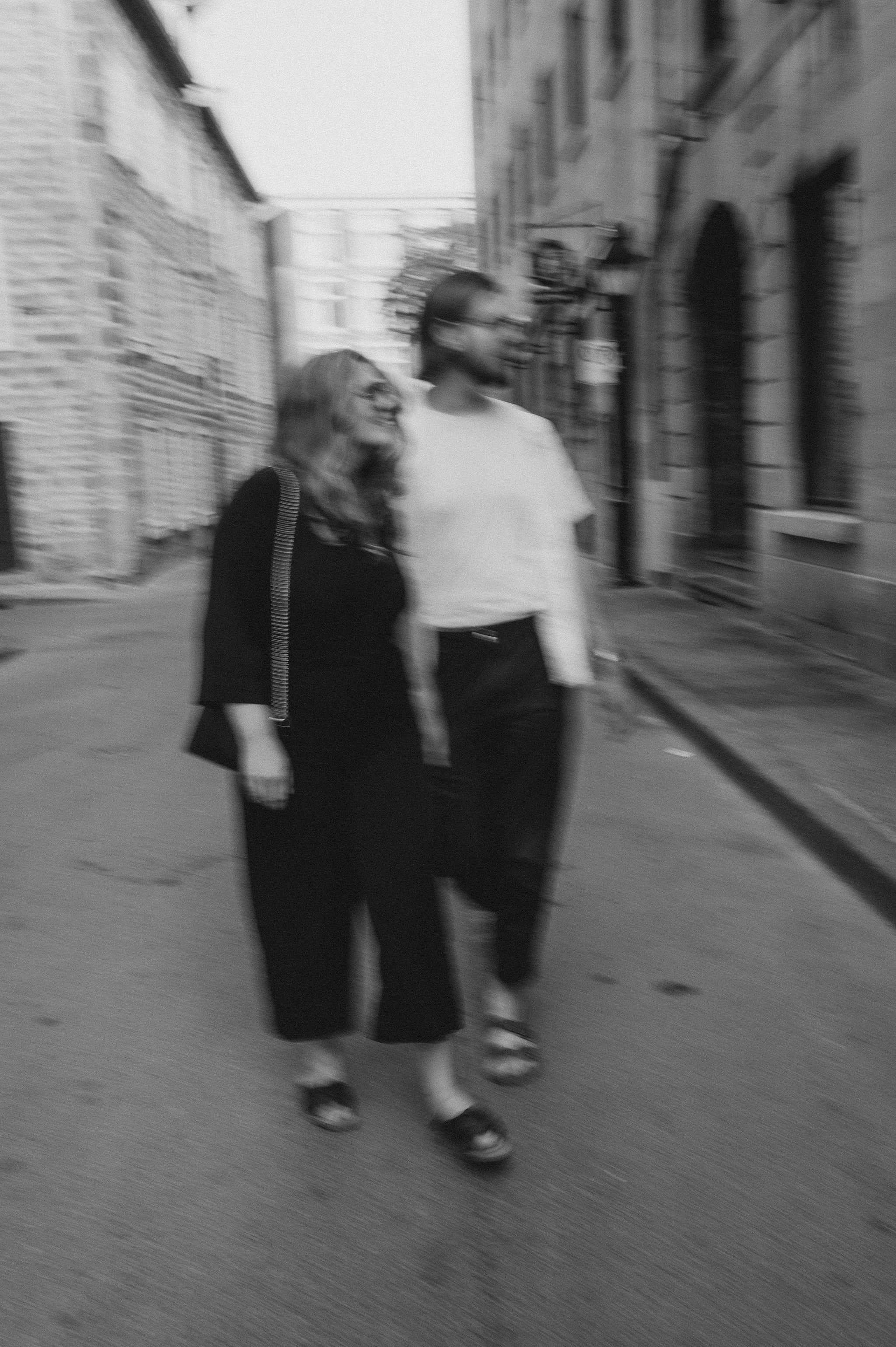 Two people walking together on a city street, smiling and talking, black and white photo, slightly blurred.