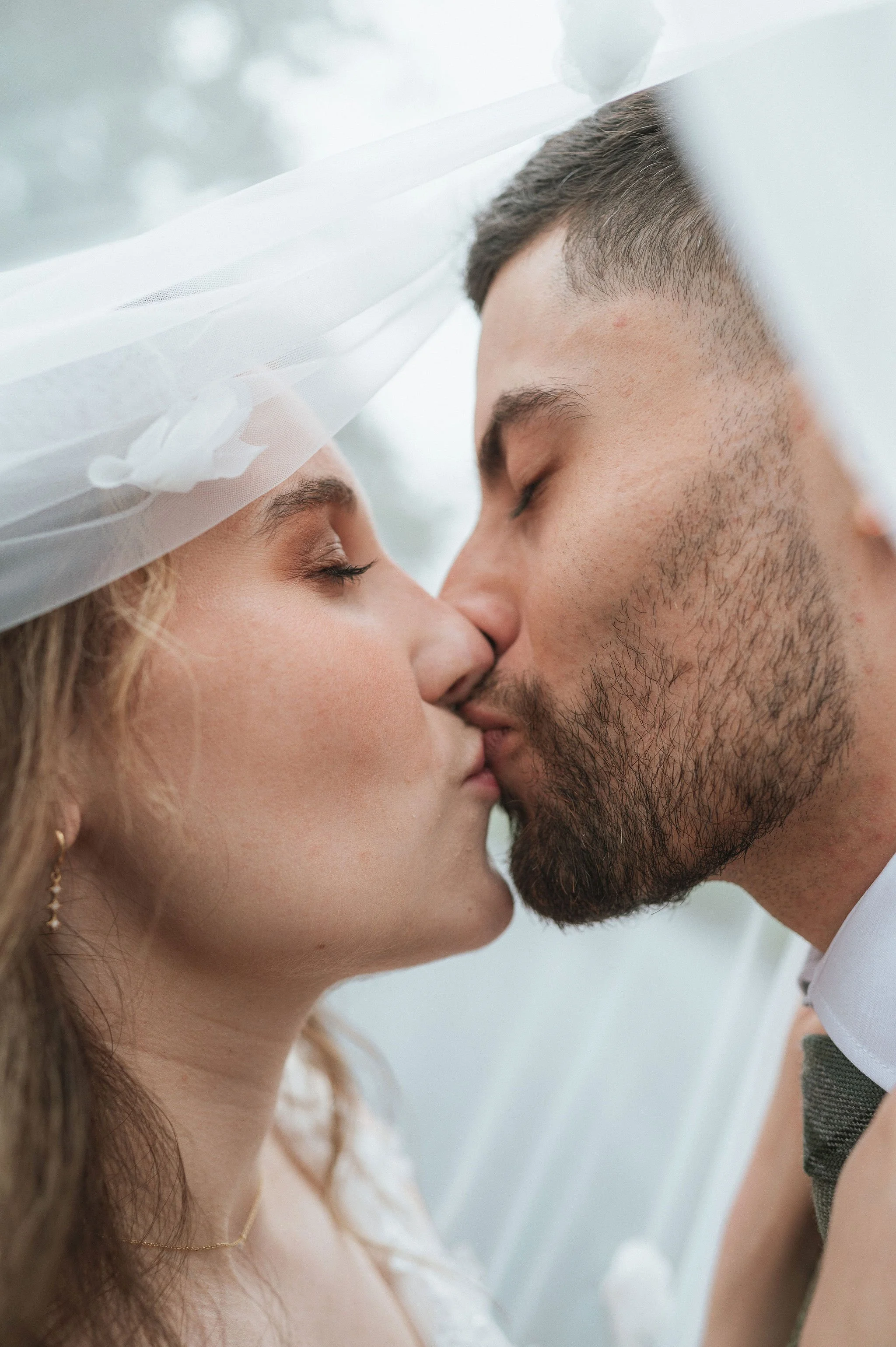 A couple kissing on their wedding day, with the bride wearing a white dress and veil, and the groom in a suit with a bow tie.