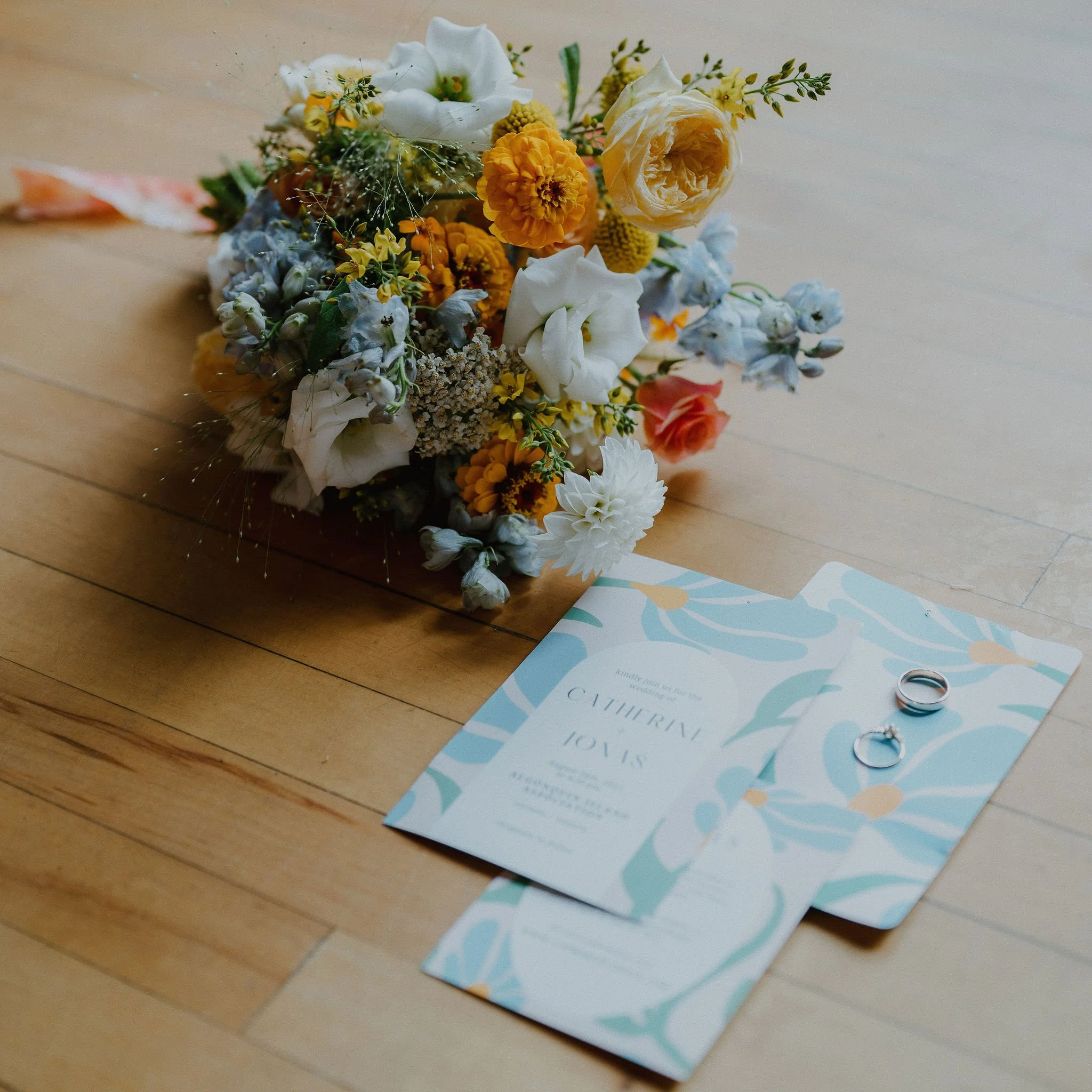 A bouquet of colorful flowers and wedding rings on a wooden floor.