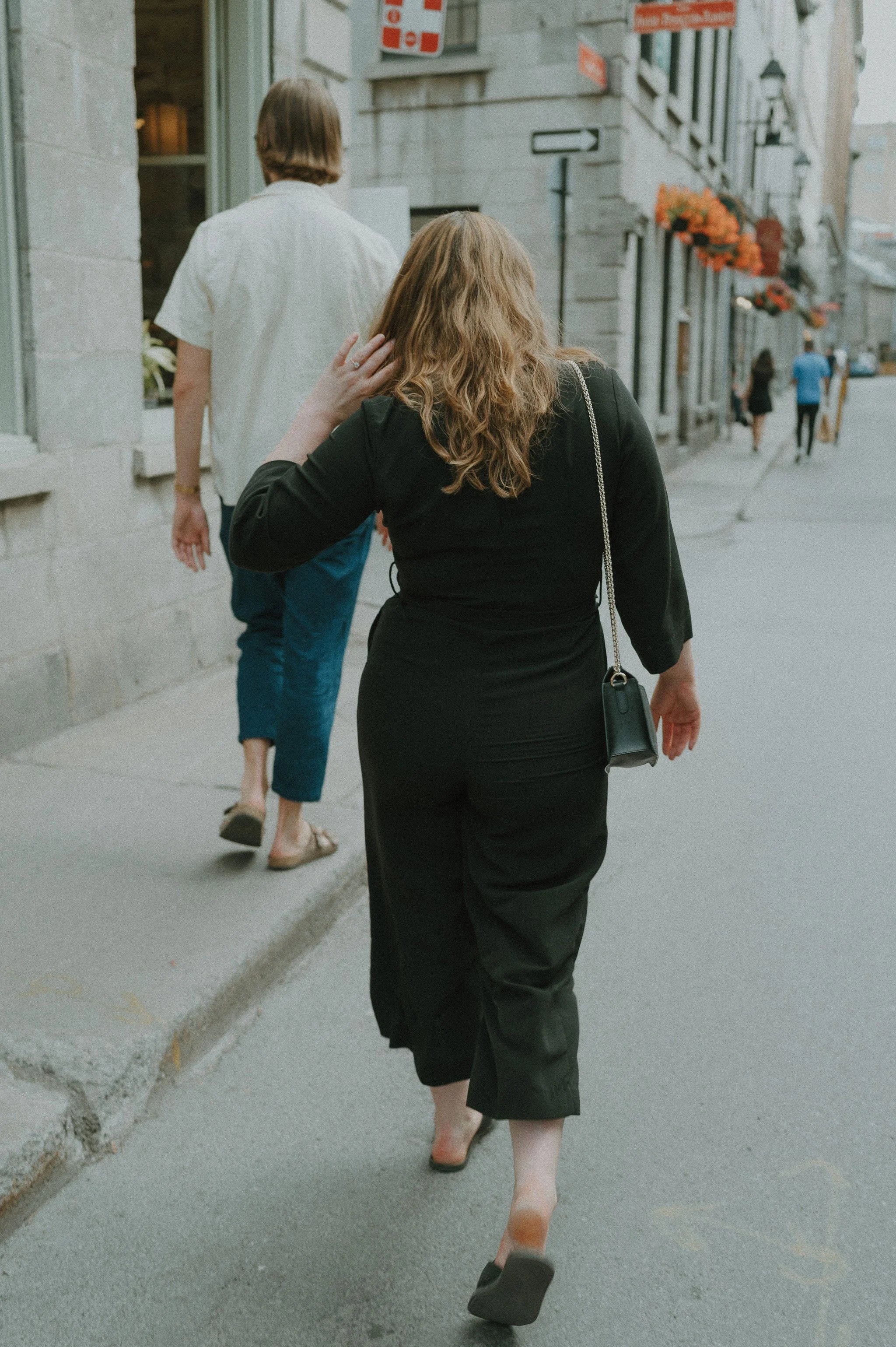 Woman in black dress walking on city sidewalk with others in background