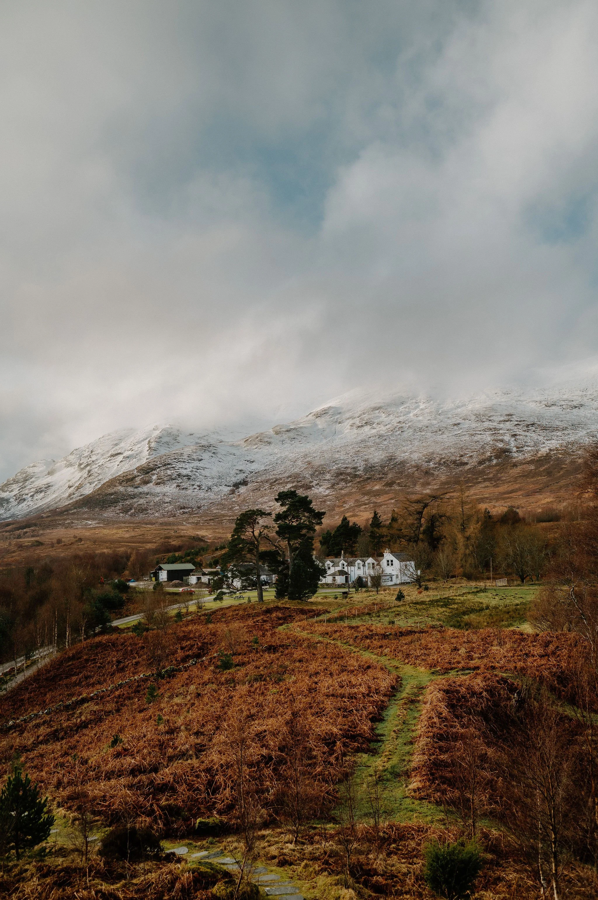 Scenic view of a mountain with snow, a small village with white houses, and a winding path through brownish vegetation.