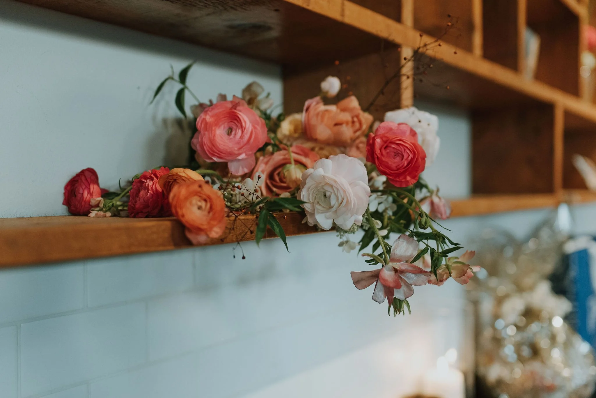 A floral arrangement of pink, white, and peach roses and other flowers draped on a wooden shelf against a light blue wall.