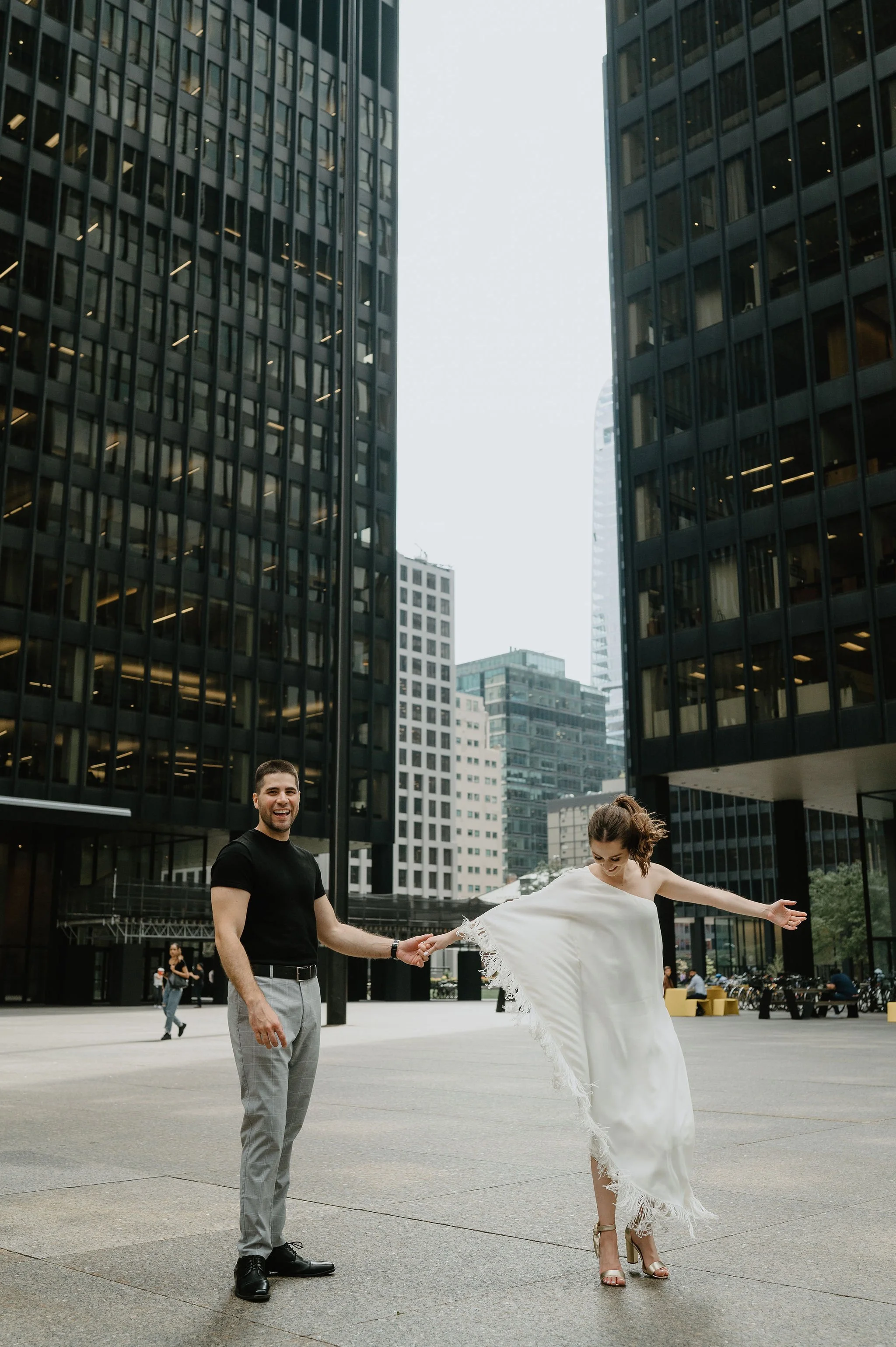 A happy couple holding hands and dancing with the city skyline behind them.