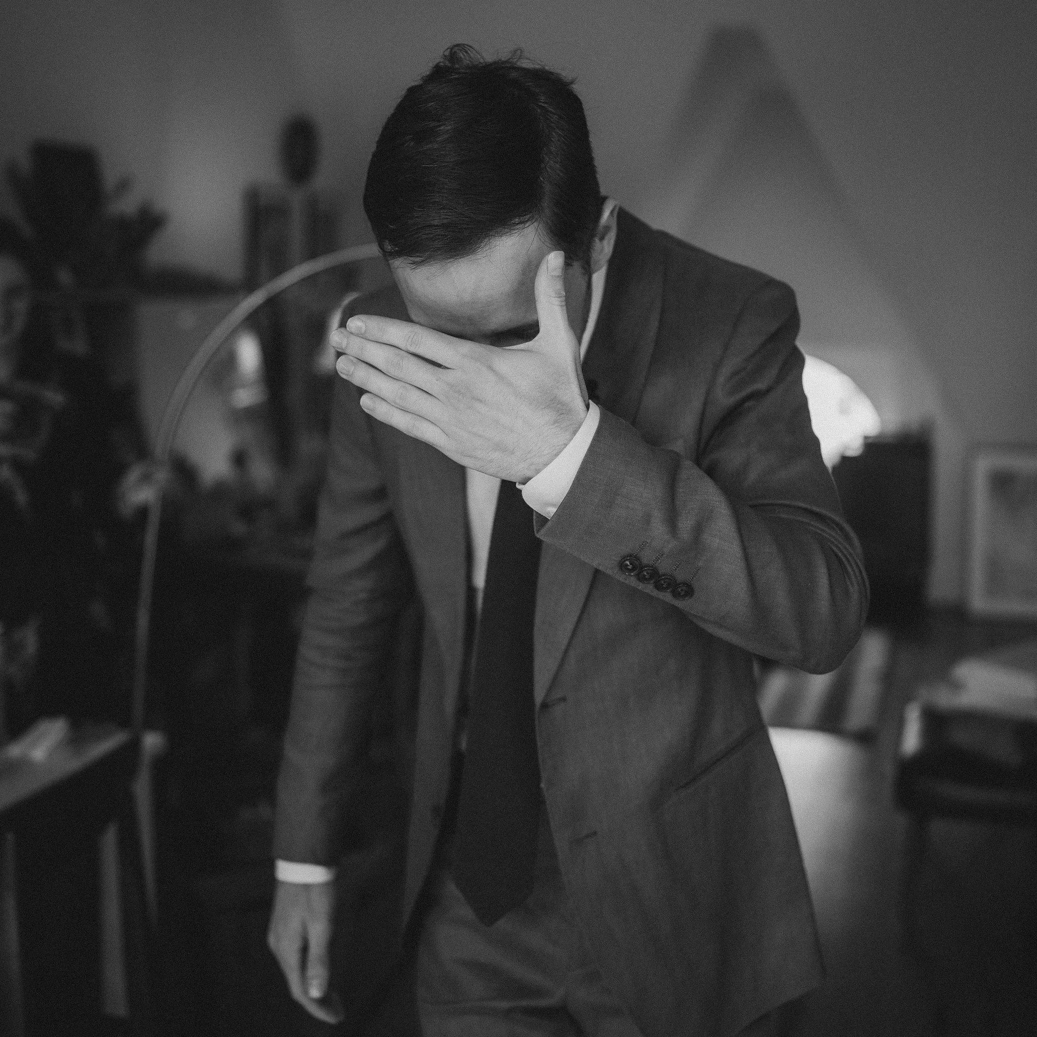 A man in a suit covering his face with his hand in an indoor setting.