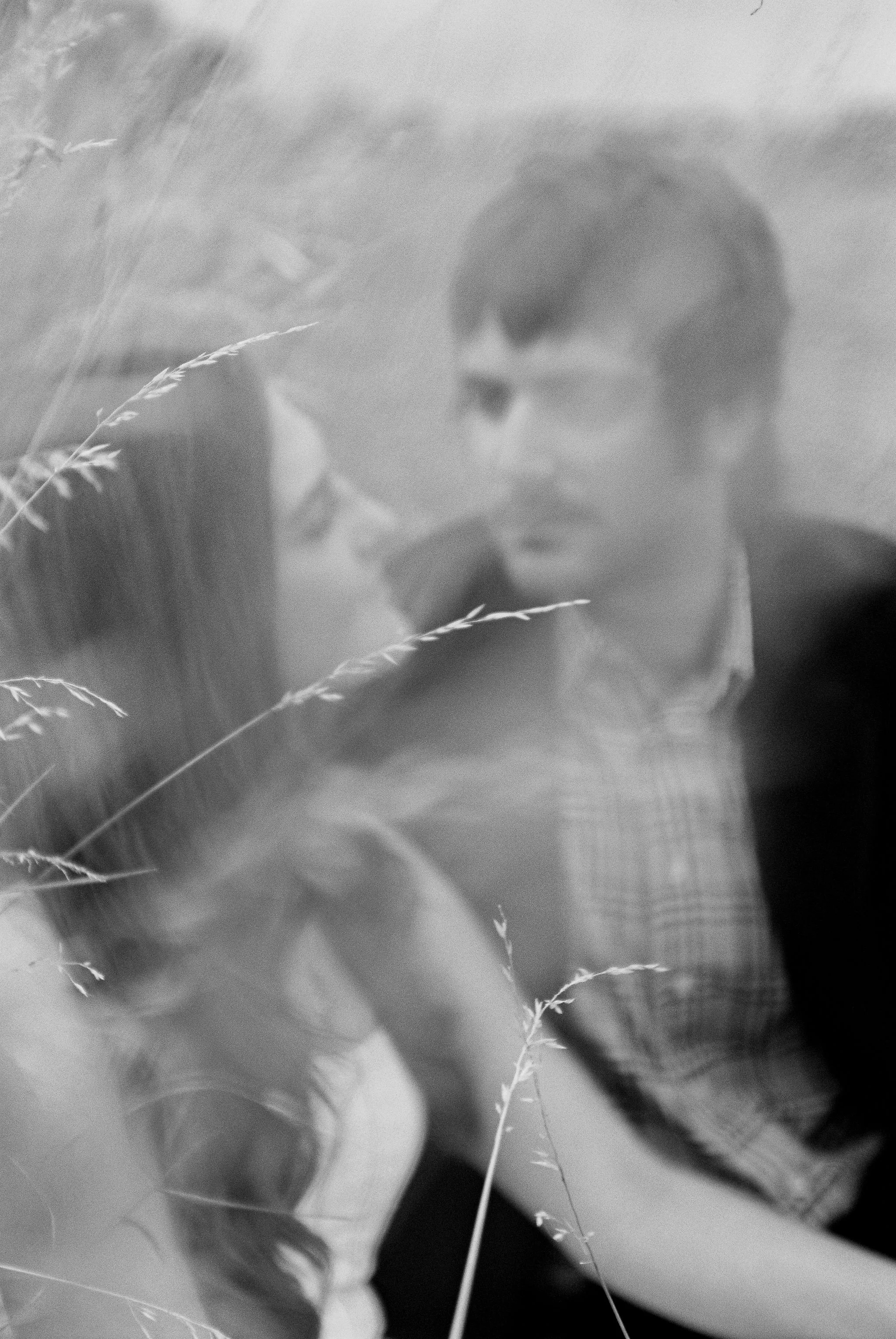 A black and white photo of a young man and woman looking at each other, with grass in the foreground.