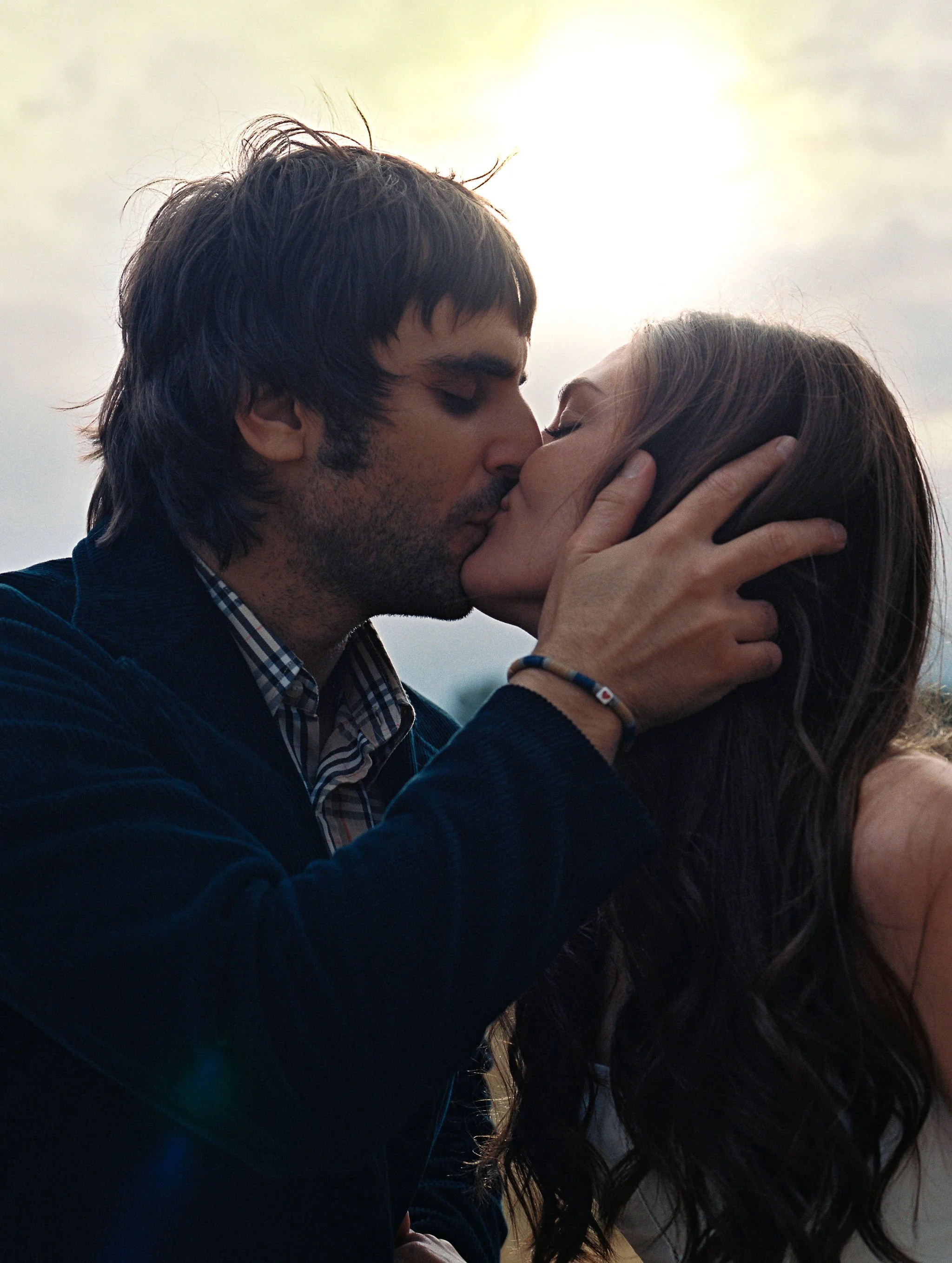 A man and woman sharing a kiss outdoors during sunset.