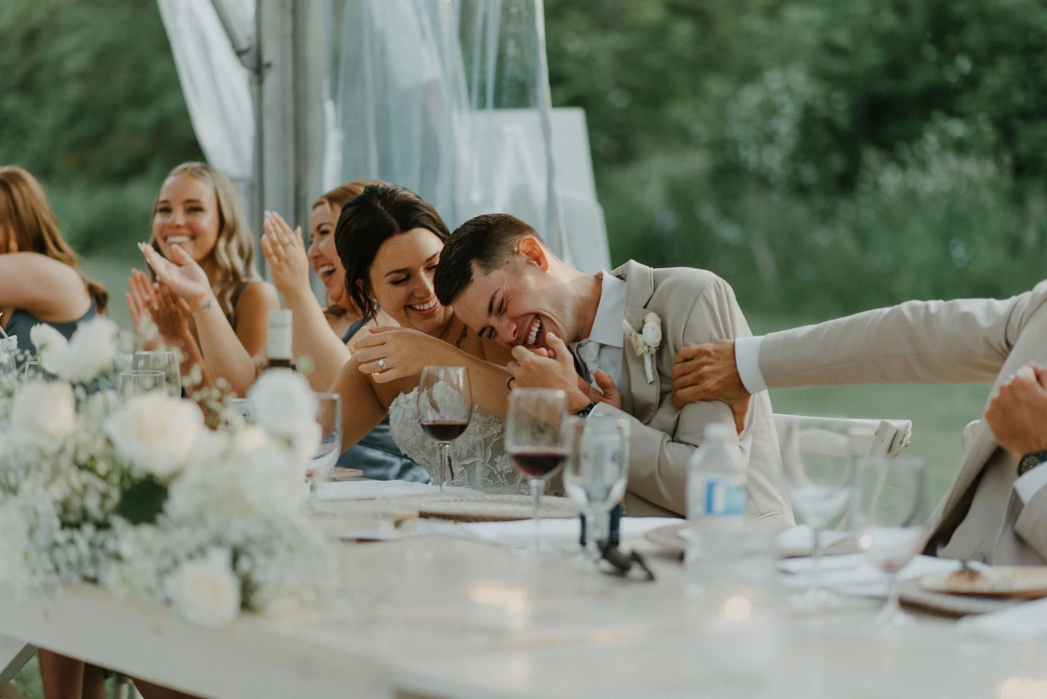 A group of people in formal attire celebrating at a wedding reception, with a man and woman in the center laughing and enjoying the moment.
