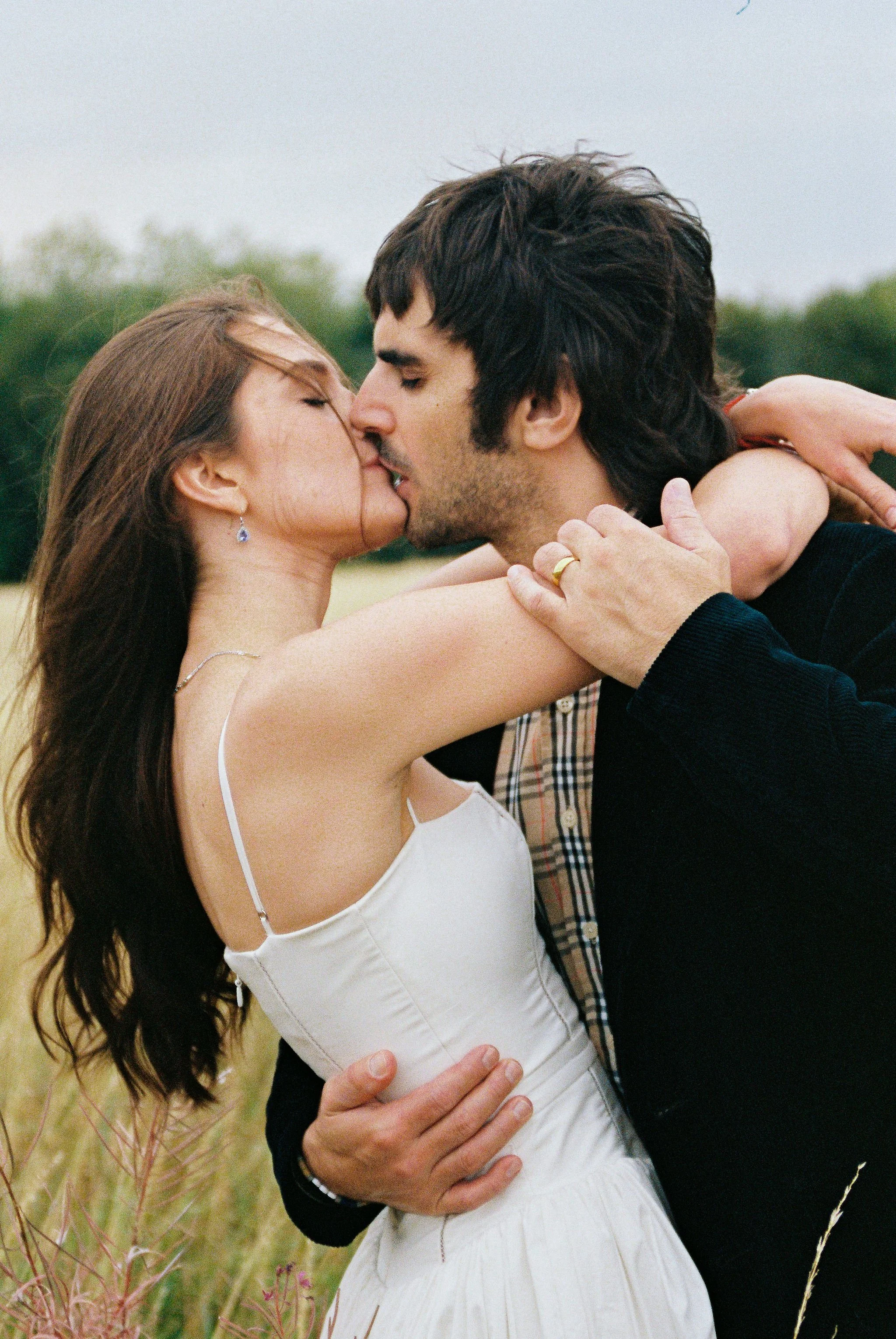 A couple in an outdoor field sharing a kiss, embracing each other.