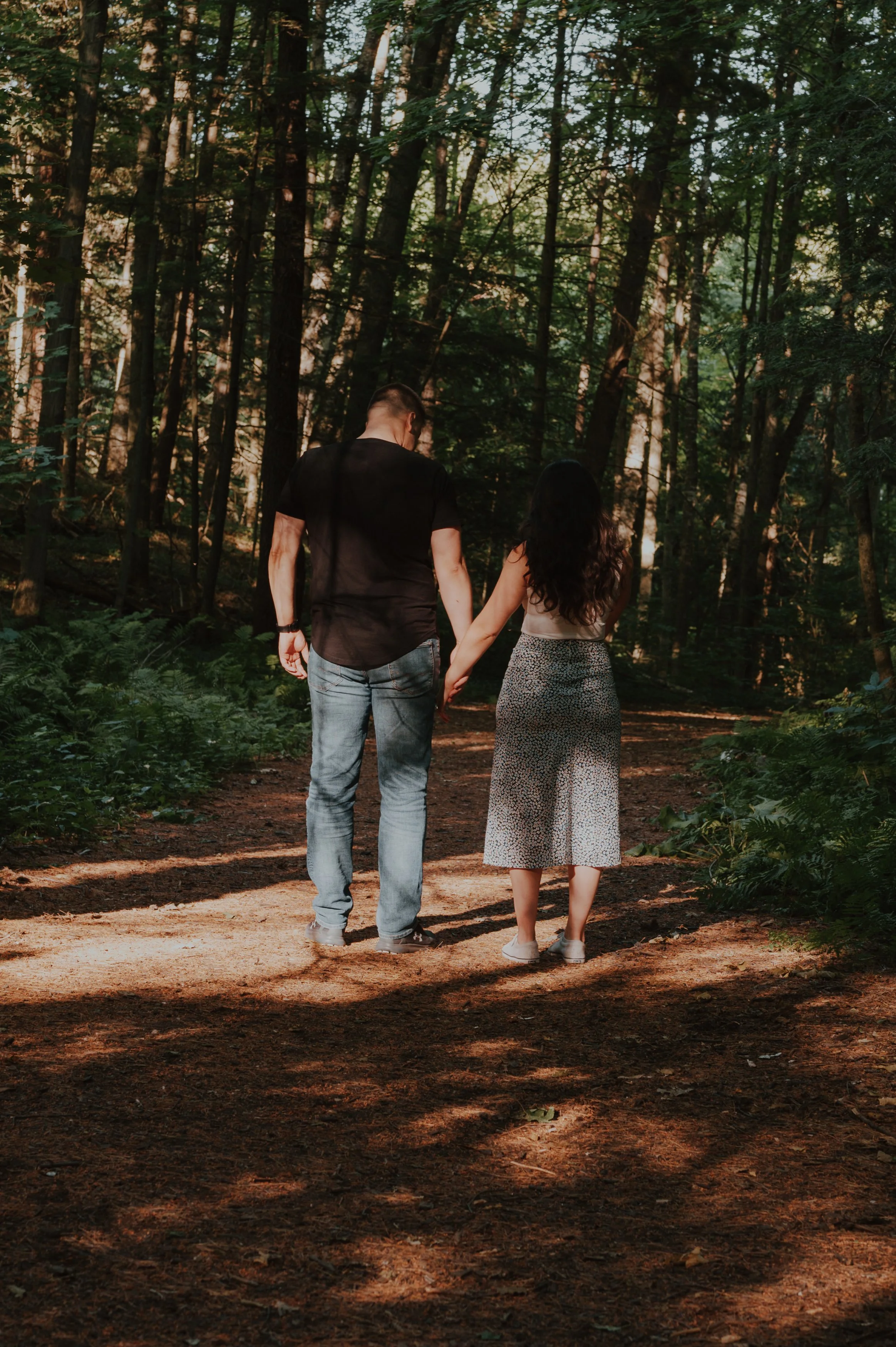 A couple walking hand-in-hand through a forest on a sunny day.