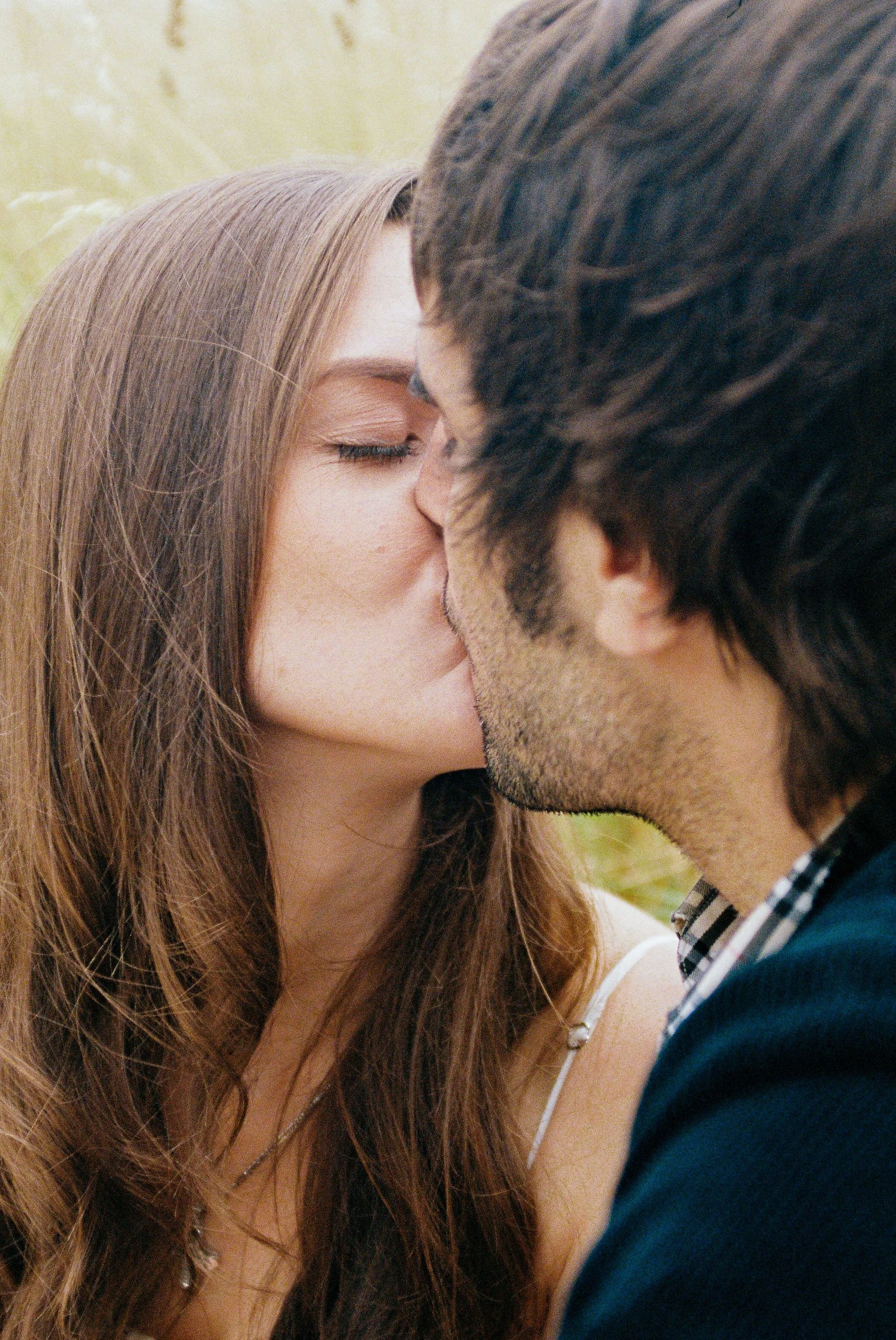 A man and woman kissing outdoors with a blurred natural background.