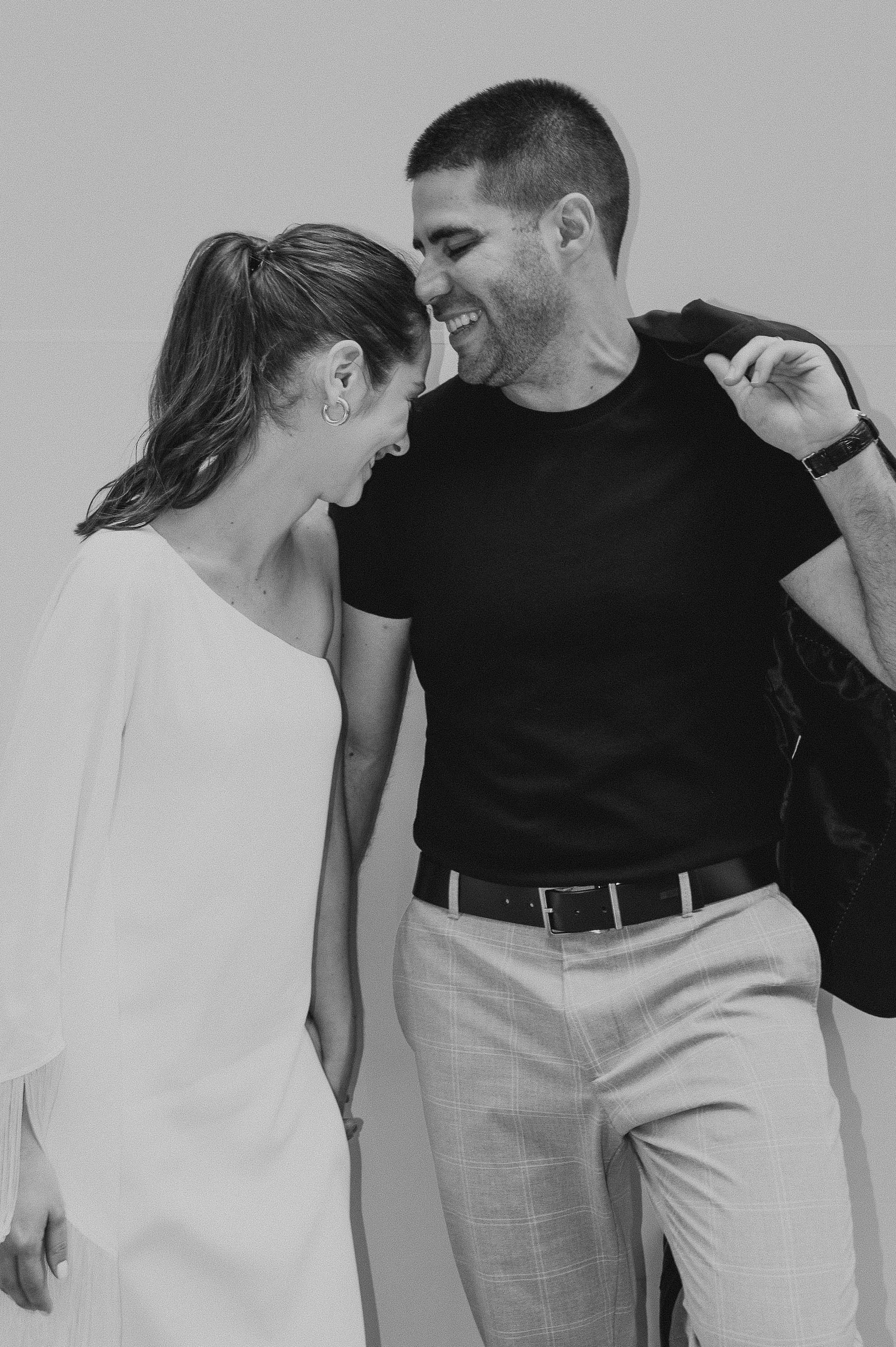 A black and white photo of a man and woman sharing a close, happy moment with their foreheads touching and smiling.