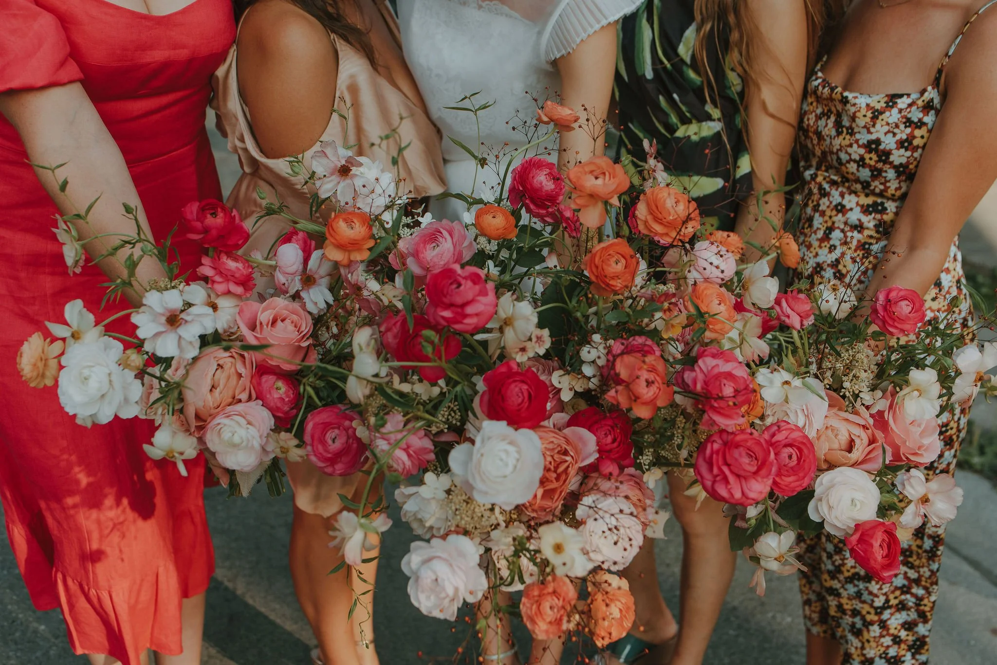 Four women holding a large bouquet of various pink, white, and orange flowers.