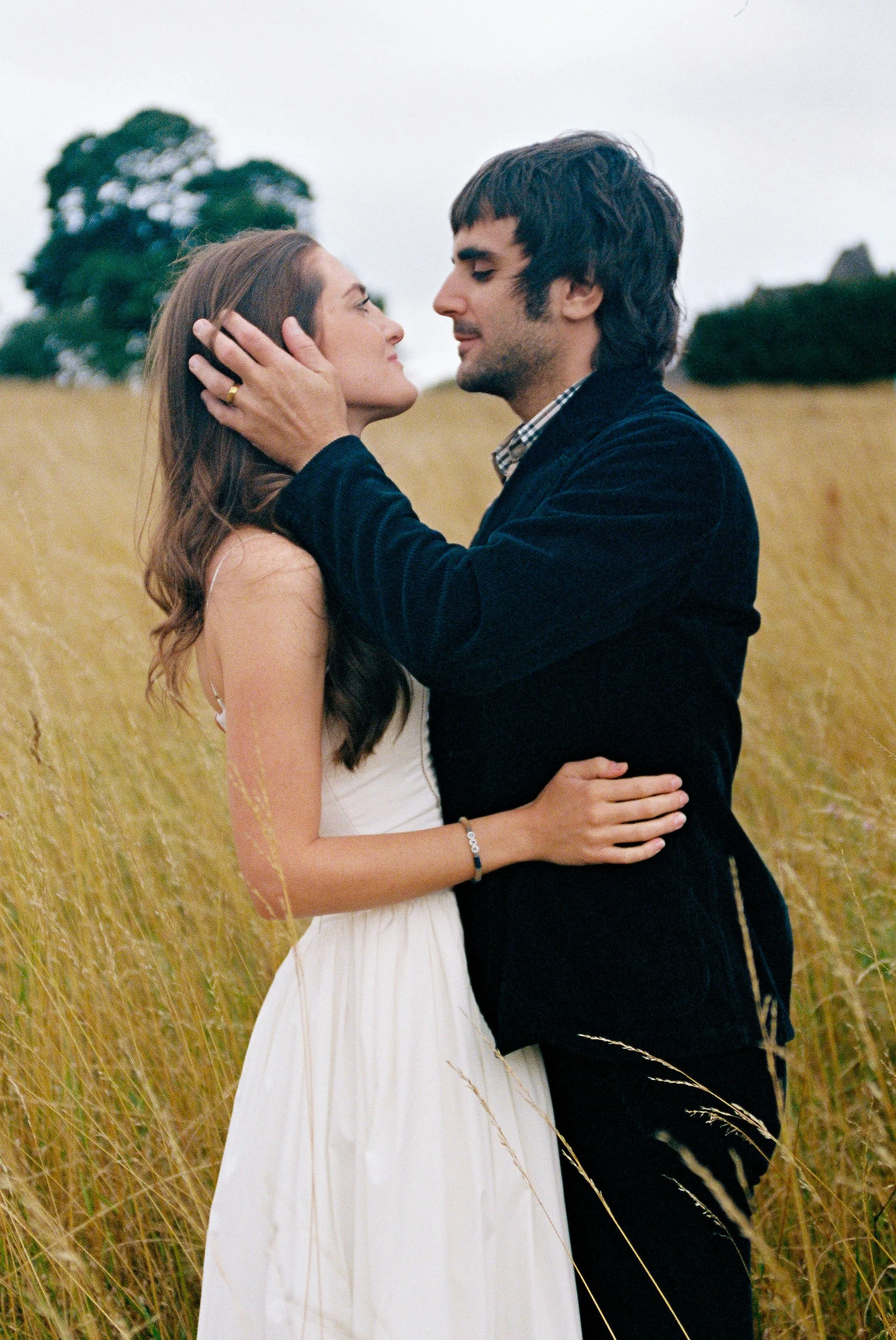 A couple embracing in a field of tall grass, looking into each other's eyes.