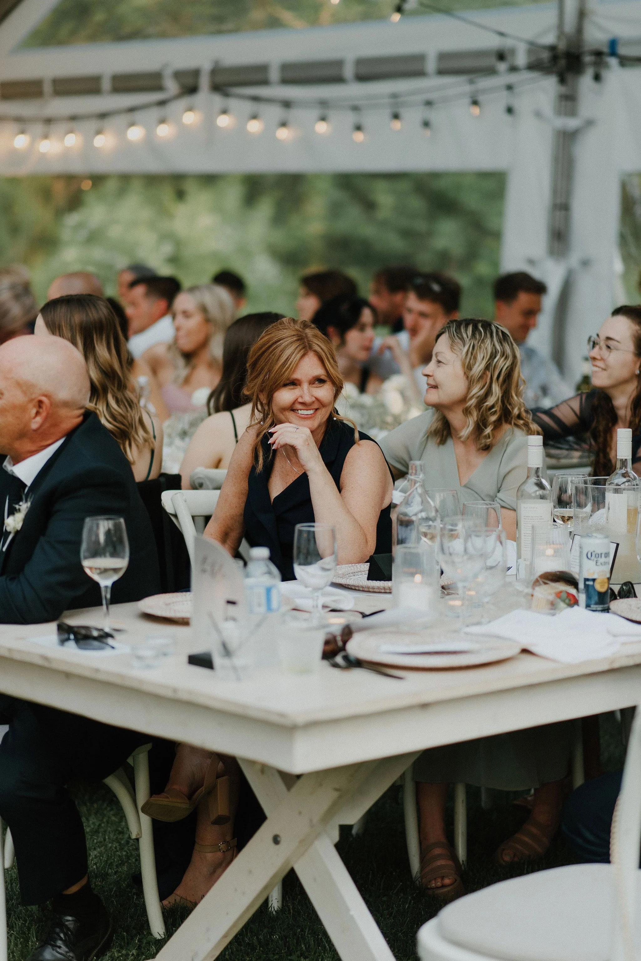 People sitting at a decorated outdoor event table, smiling and engaging, with string lights overhead.