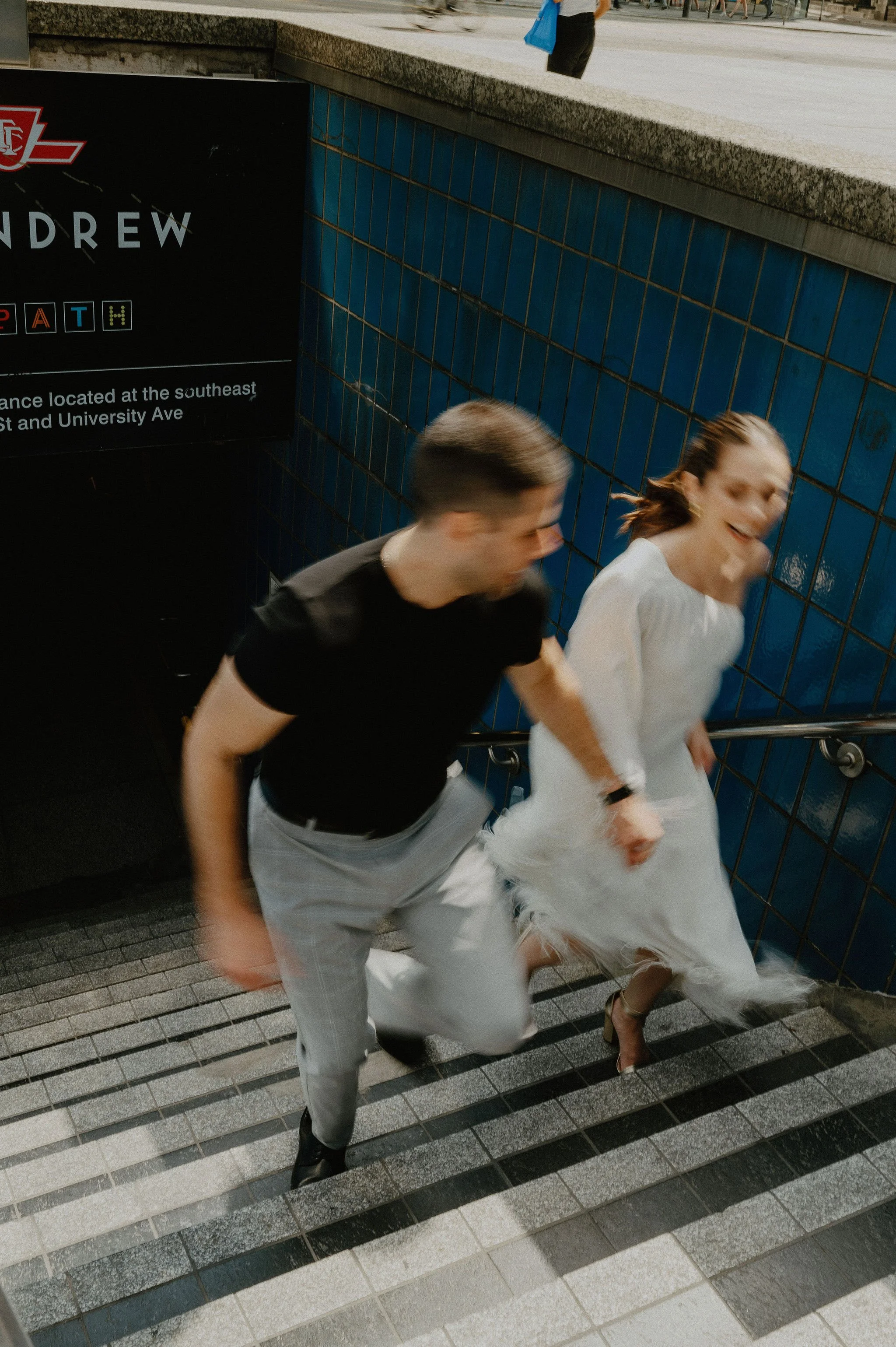 A man and woman are running up a staircase in a subway station, both smiling and appearing joyful.