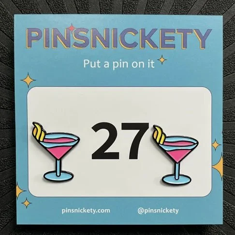 Collection of "Pinsnickety" custom enamel pins with blue ribbon design on packaging