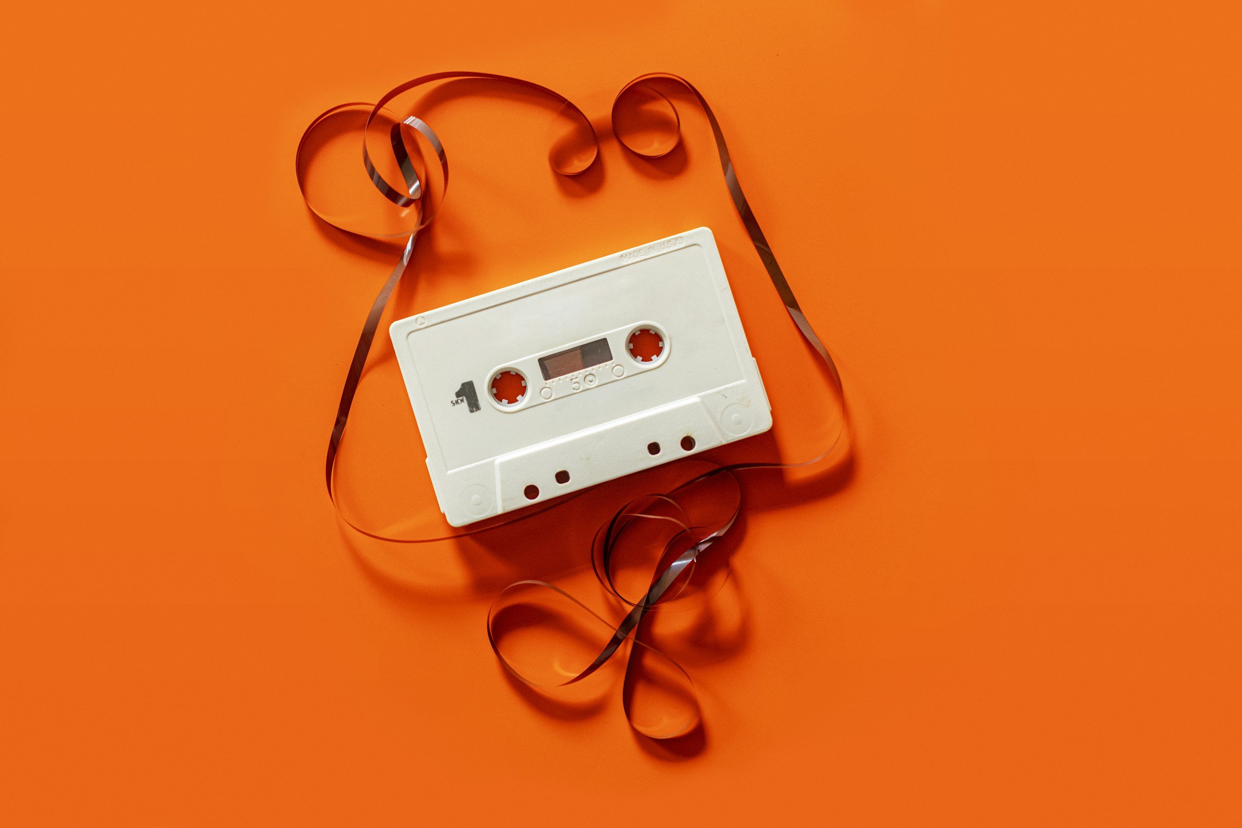 A white cassette tape with a black ribbon lying on an orange background.