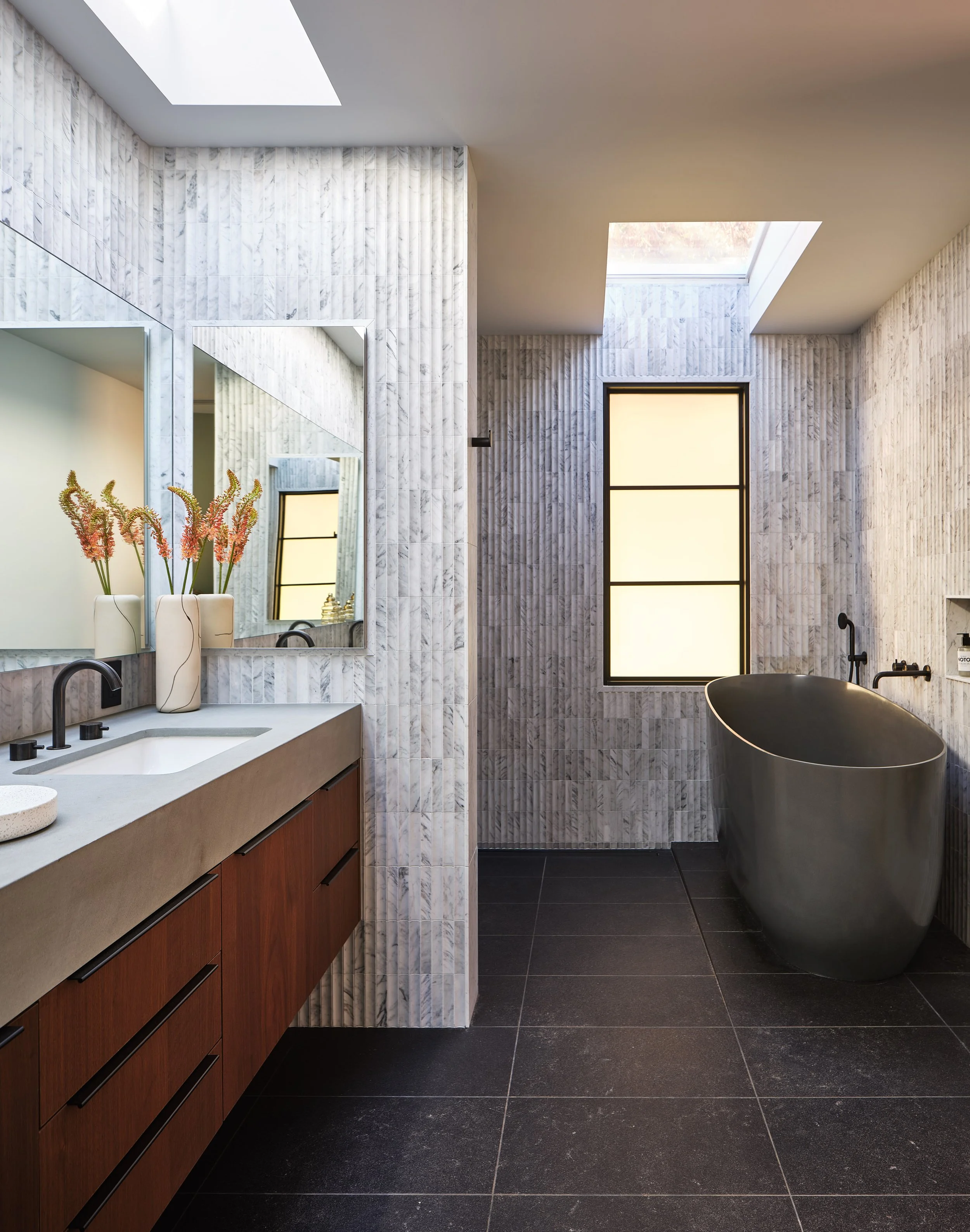 Skylit primary bathroom with warm wood and stone finishes