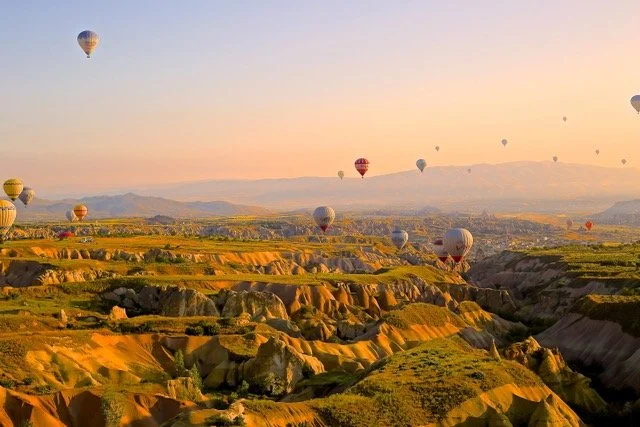 Several hot air balloons floating in the sky at sunset. Beautiful orange glow illuminates majestic mountains in the background, creating a peaceful scenery of an evening flight.