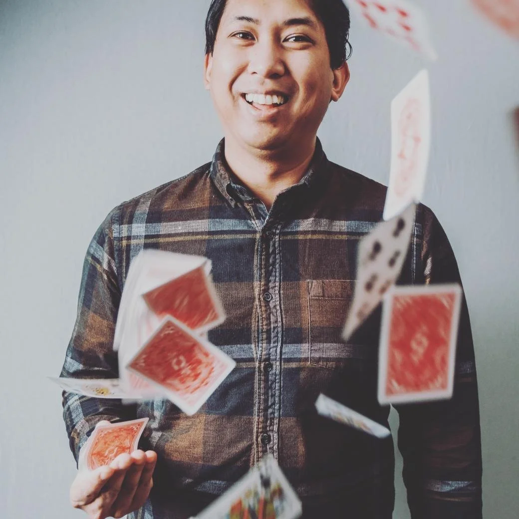 A man smiling while playing with falling red and white playing cards.