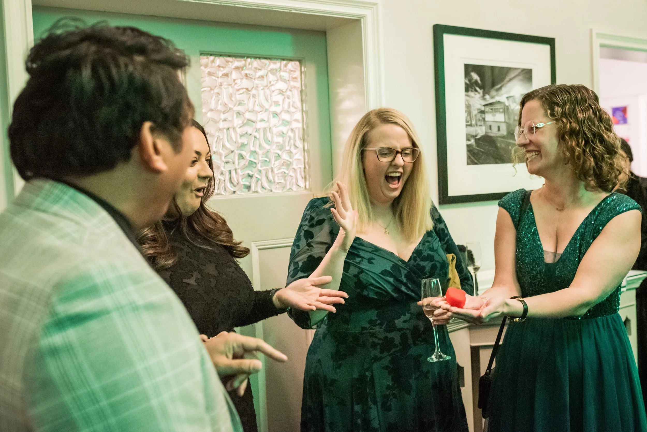 Group of people at a social gathering, smiling and engaging in conversation, with some holding glasses of wine.
