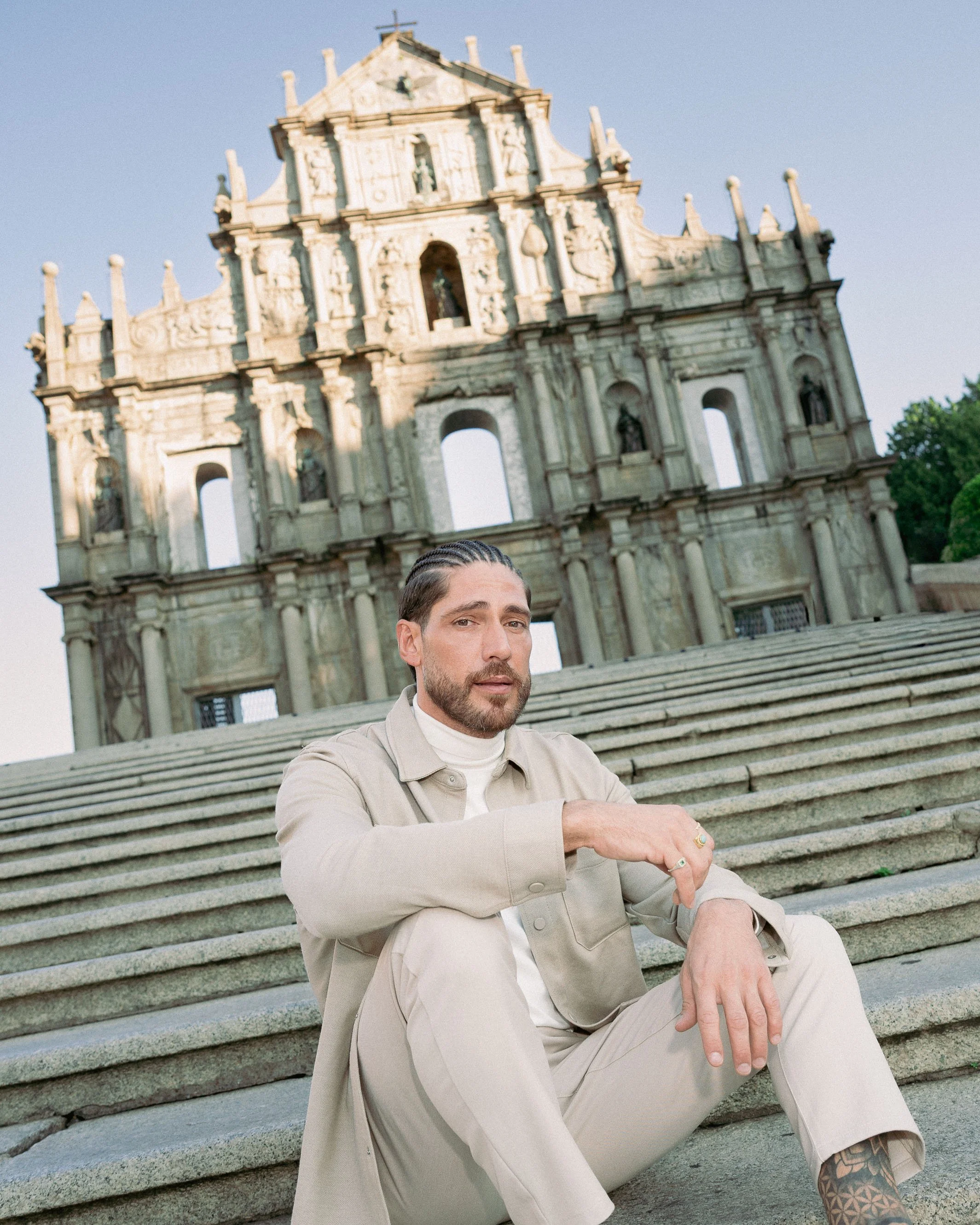 Environmental portrait of Angelo Rodrigues framed by the Ruins of St. Paul’s, Macau, blending historic architecture and contemporary styling. Retrato ambiental de Angelo Rodrigues enquadrado pelas Ruínas de São Paulo, em Macau, combinando arquitetura