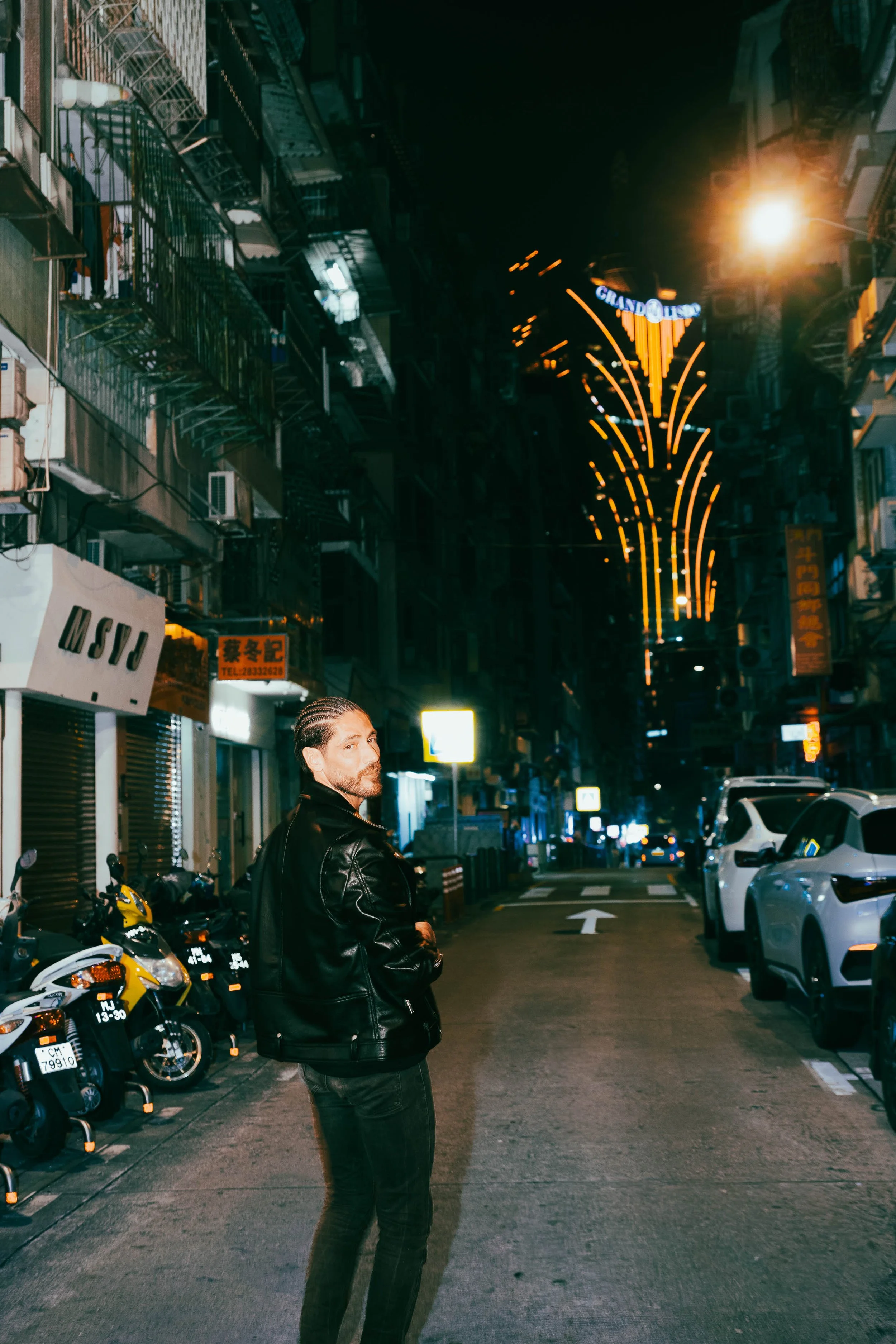 Urban fashion portrait of Angelo Rodrigues at night in Macau, photographed near Grand Lisboa with neon signage and city reflections. Retrato urbano de moda de Angelo Rodrigues à noite em Macau, fotografado junto ao Grand Lisboa com letreiros néon e r