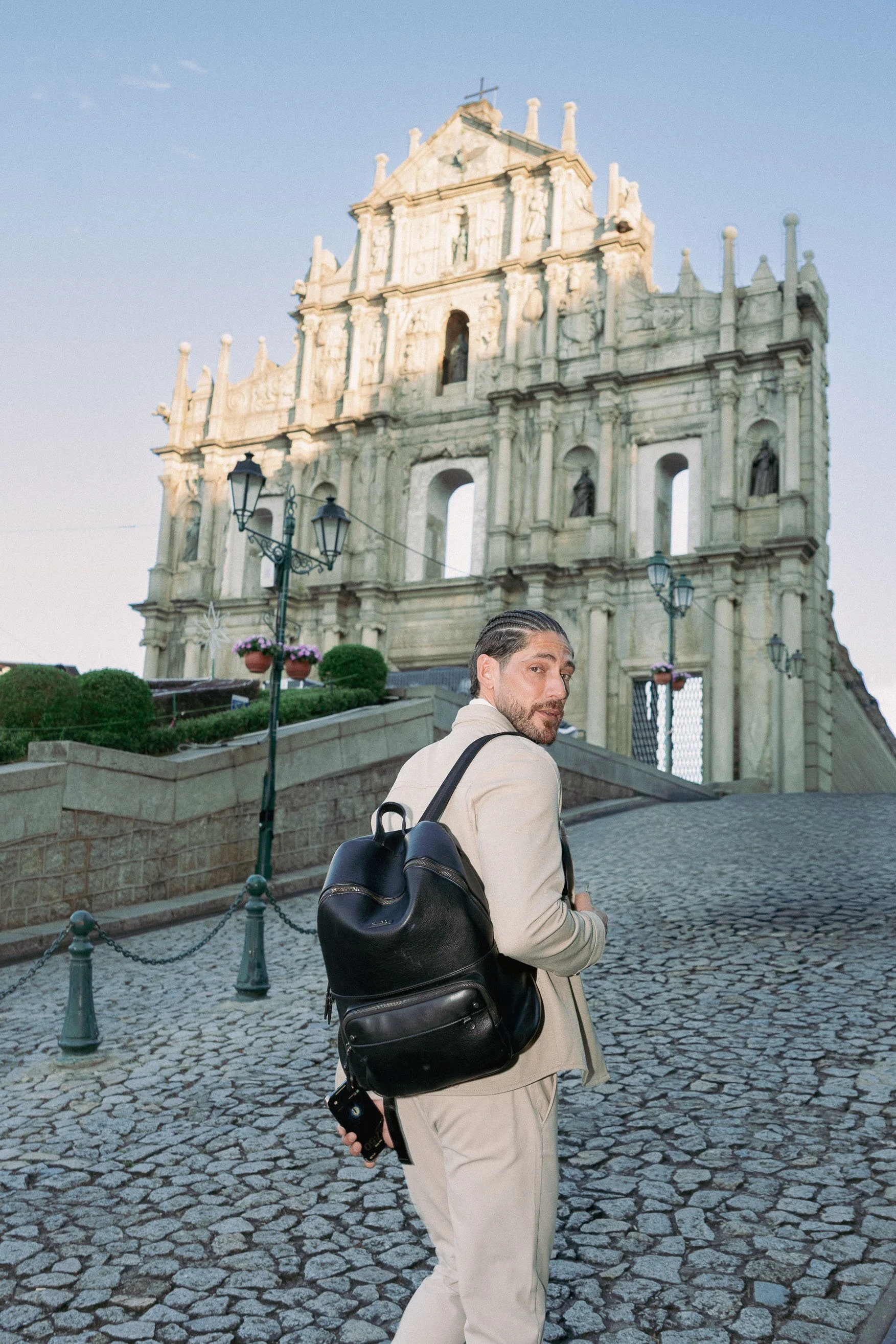 Wide portrait of Angelo Rodrigues at the Ruins of St. Paul’s, Macau, highlighting scale, historic steps, and architectural context. etrato em plano aberto de Angelo Rodrigues nas Ruínas de São Paulo, em Macau, destacando a escala, as escadarias histó