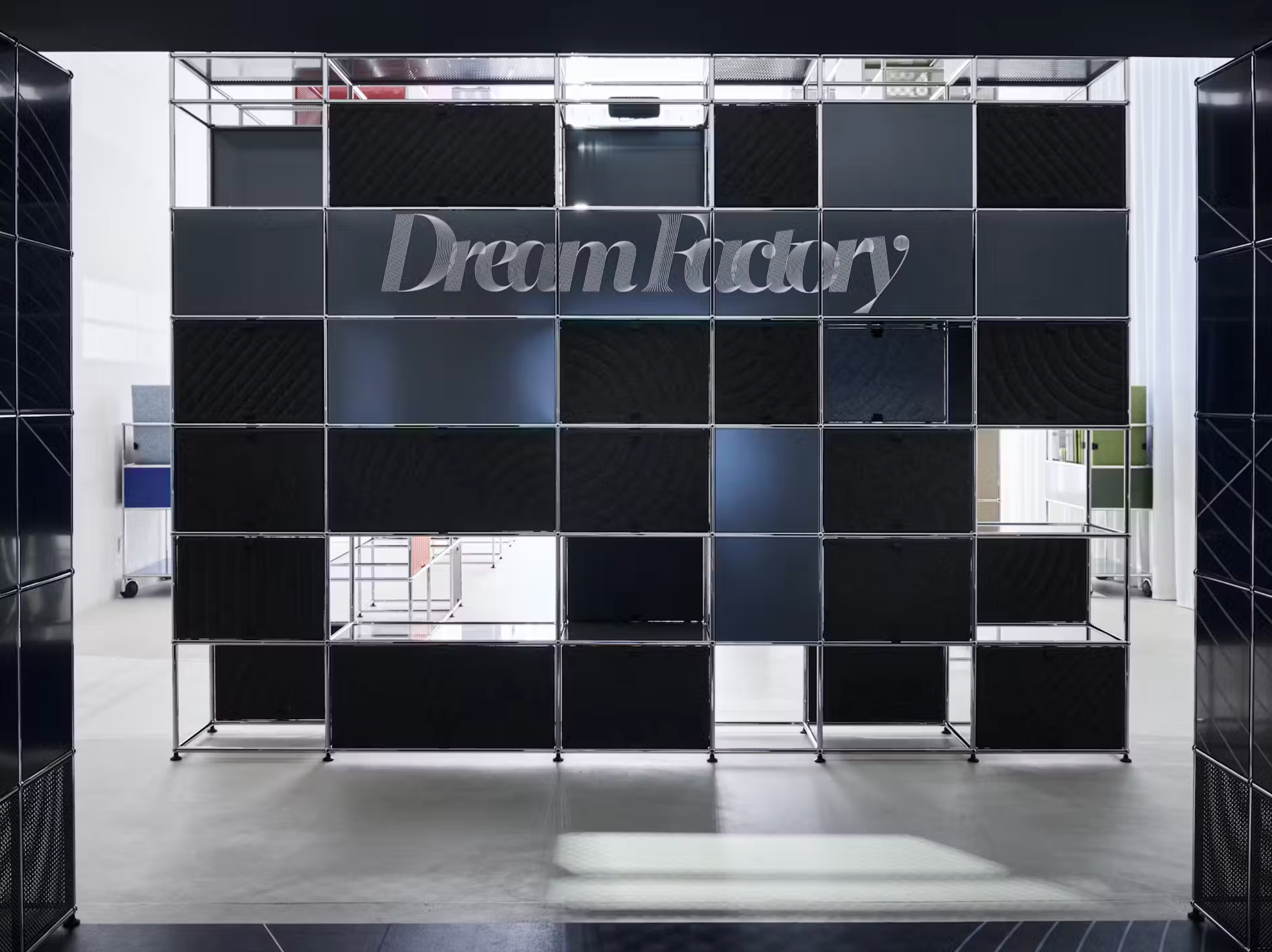 Interior view of a modern building with a black grid shelving unit with the words 'Dream Factory' on it, and a clear corridor leading to other rooms.