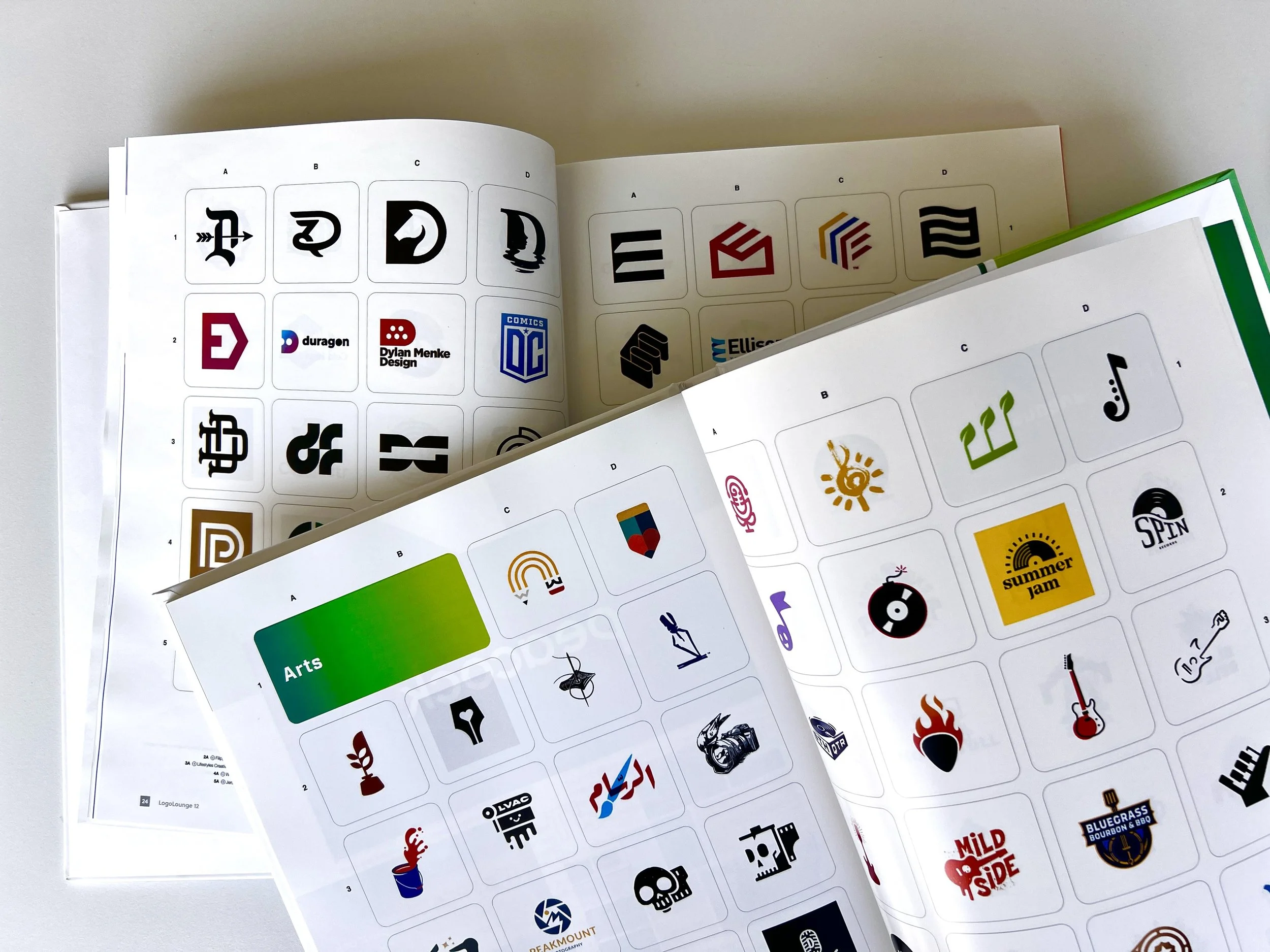Open books displaying various logos and icons on pages, categorized into sections like 'Arts' and others, with some logos for brands, music, and entertainment.