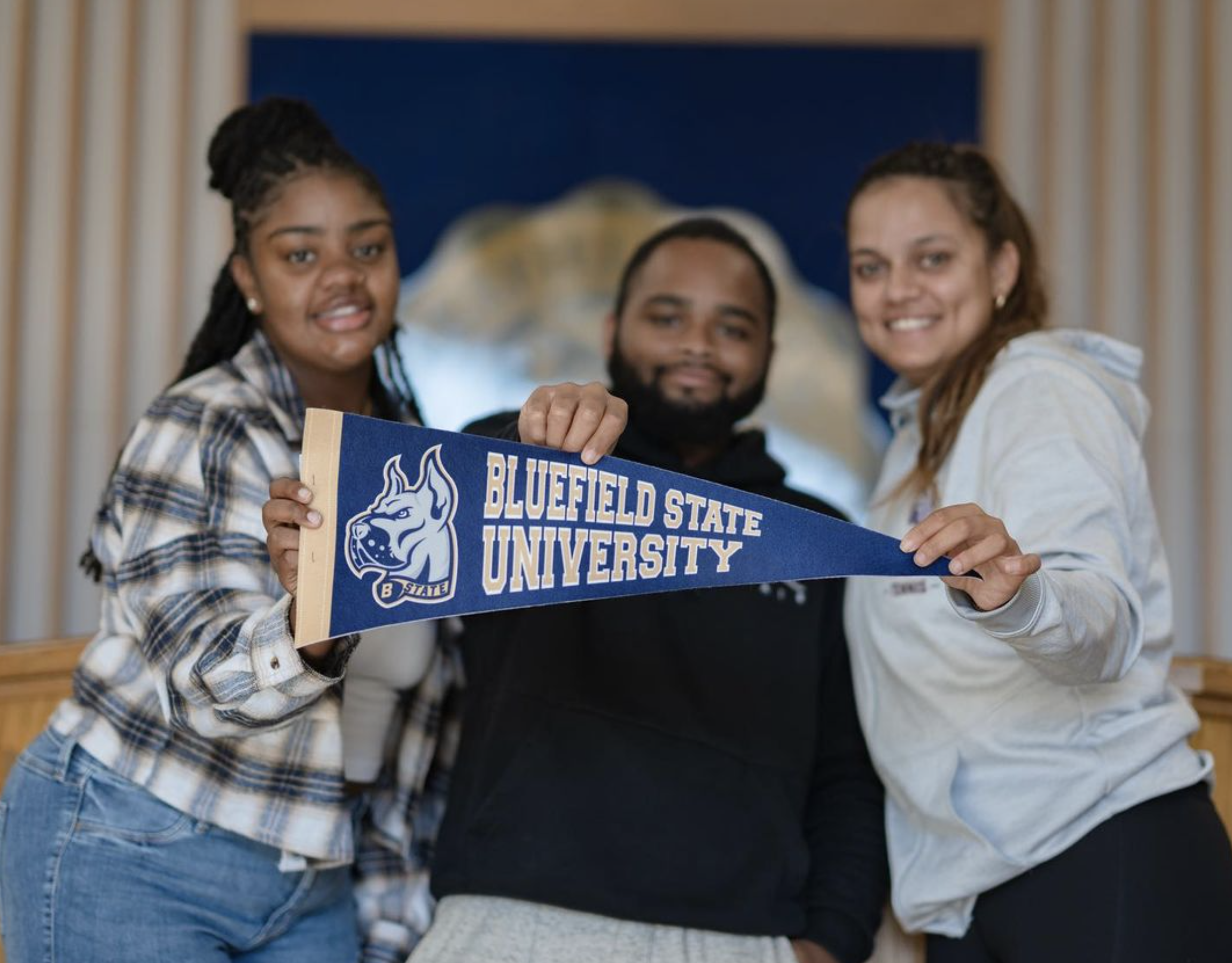Three people holding a Bluefield State University pennant indoors.