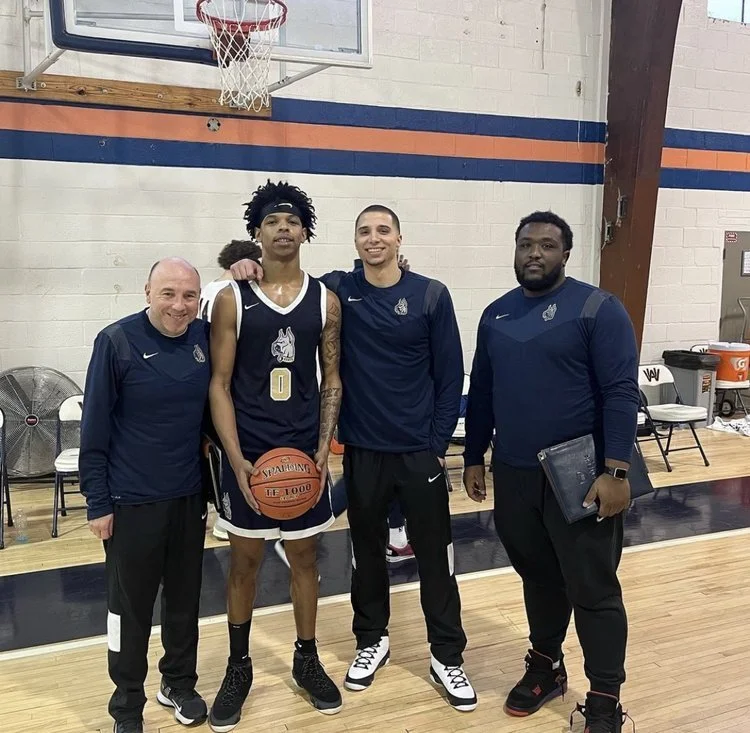 Four people at a basketball court. One is a player holding a basketball, while the others wear similar sports apparel, posing together.