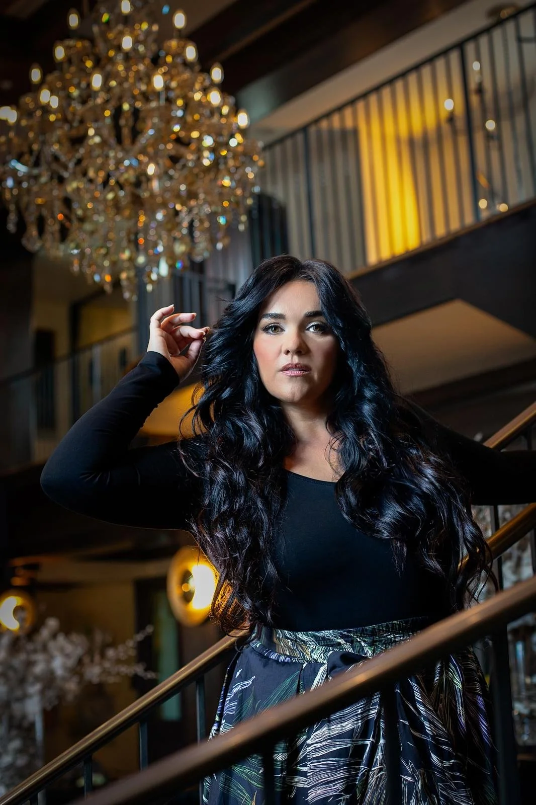 Jeanette Vecchione-Donatti in black on a staircase beneath a crystal chandelier