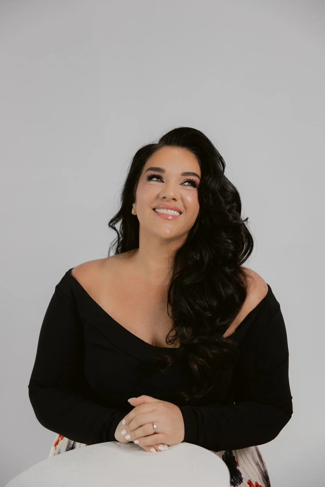 Jeanette Vecchione-Donatti in an off-the-shoulder black top, looking over her shoulder