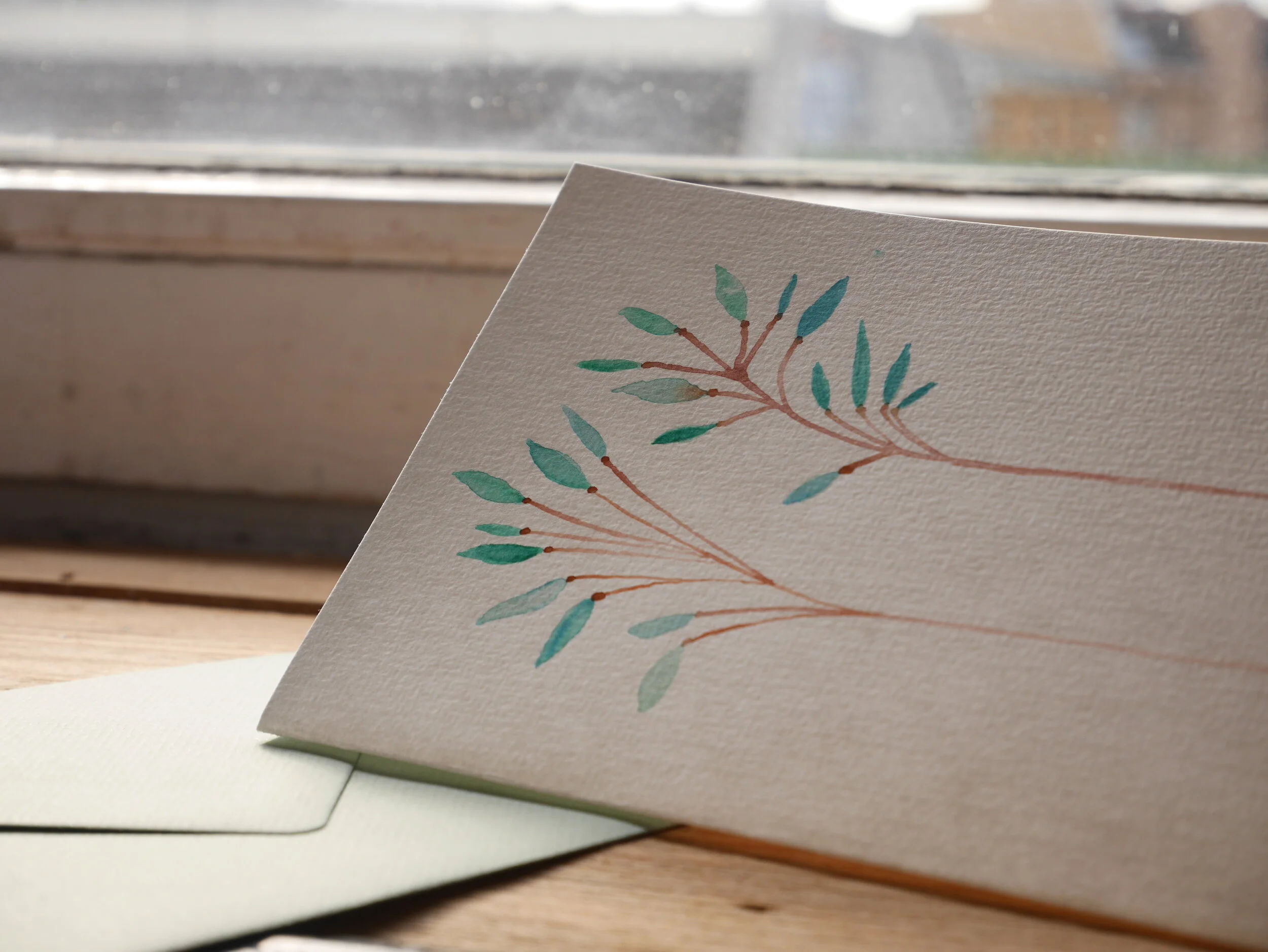 Klappkarte aus Papier mit Aquarellzeichnung und mildgrünem Umschlag Zwei zarte braune Zweige mit Pastellgrünen Blättern