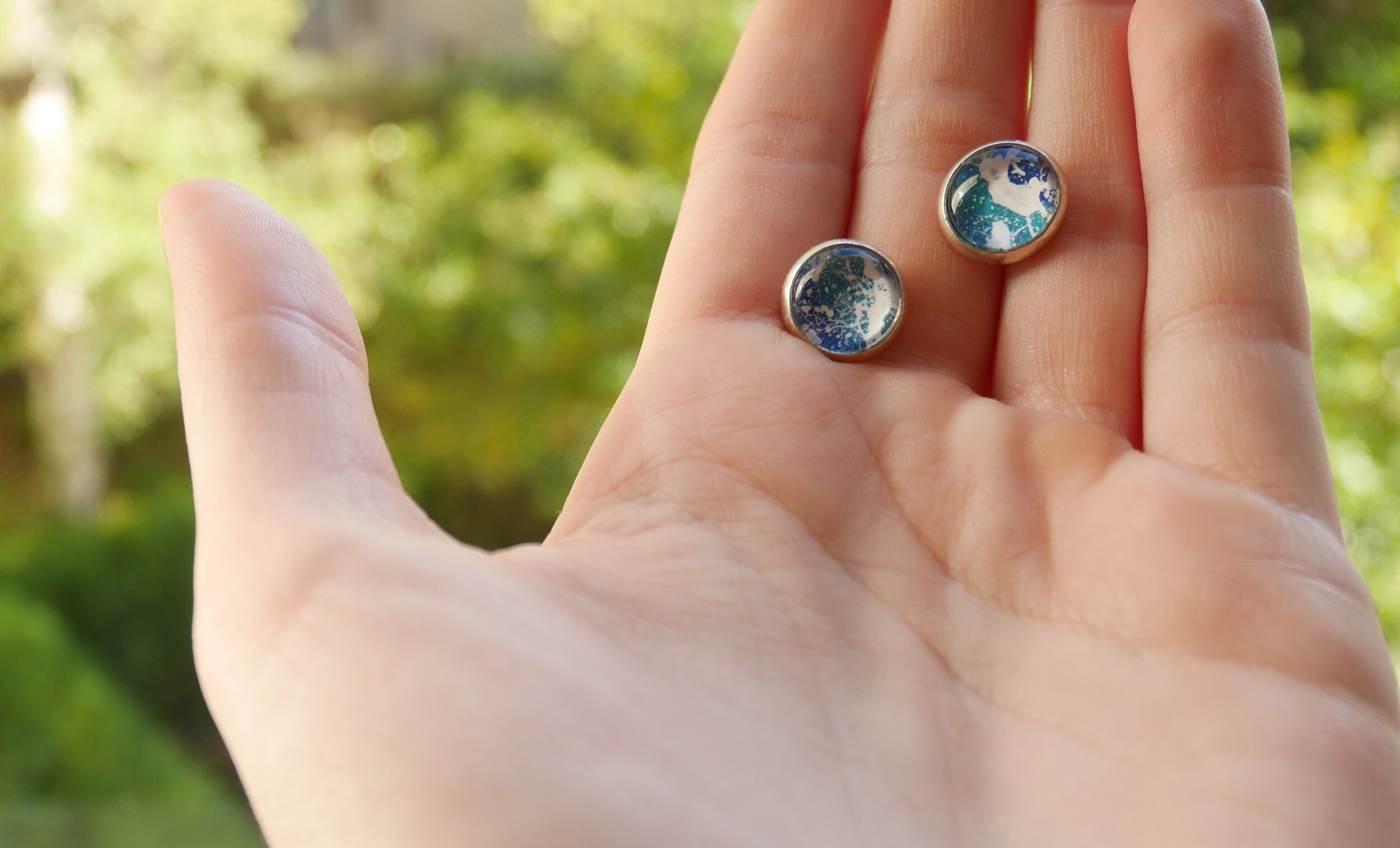 kleine, runde silberne Ohrstecker mit handbemalten Glascabochons in verschiedenen Blau- und Türkistönen und weißen Farbklecksen