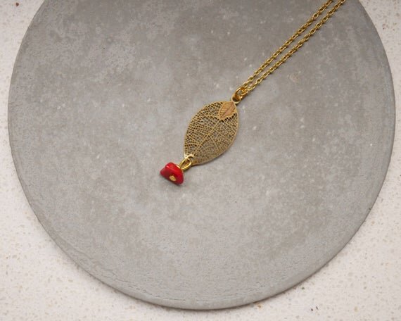 goldene Halskette mit einem filigranen Blattanhänger und einem kleinen roten Stein