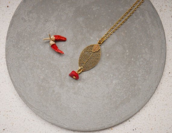 goldene Halskette mit einem filigranen Blattanhänger und einem kleinen roten Stein