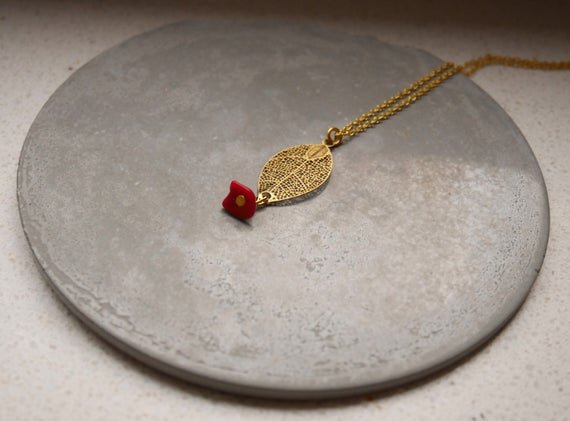 goldene Halskette mit einem filigranen Blattanhänger und einem kleinen roten Stein