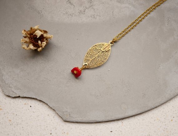 goldene Halskette mit einem filigranen Blattanhänger und einem kleinen roten Stein