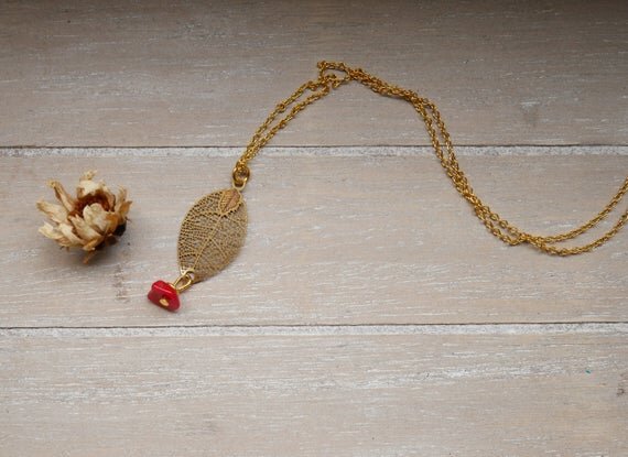 goldene Halskette mit einem filigranen Blattanhänger und einem kleinen roten Stein