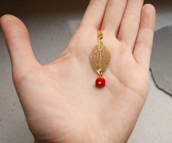 goldene Halskette mit einem filigranen Blattanhänger und einem kleinen roten Stein