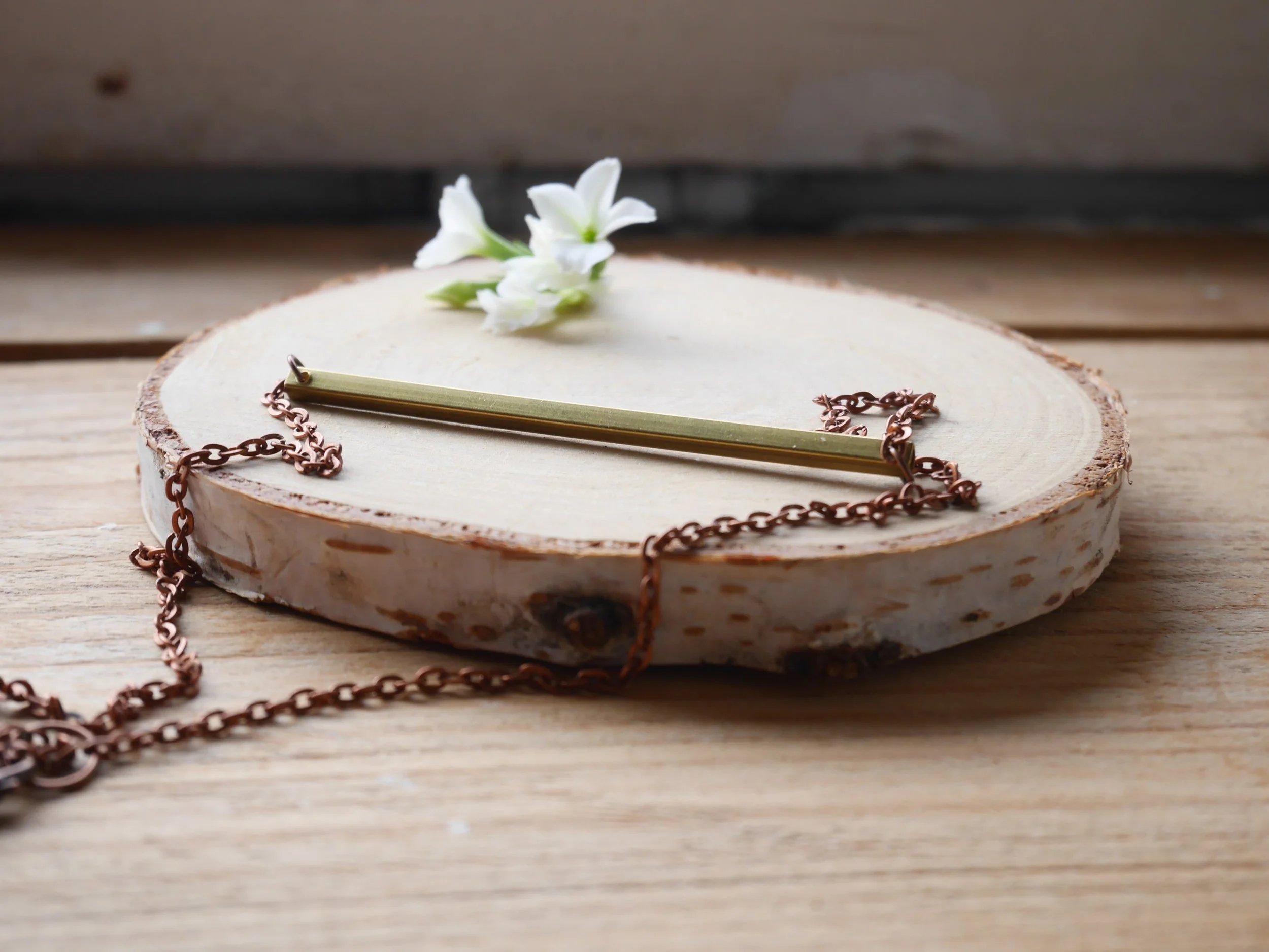 Kupferfarbene Kette mit einem waagerechten goldfarbenen Stab als Verbinder