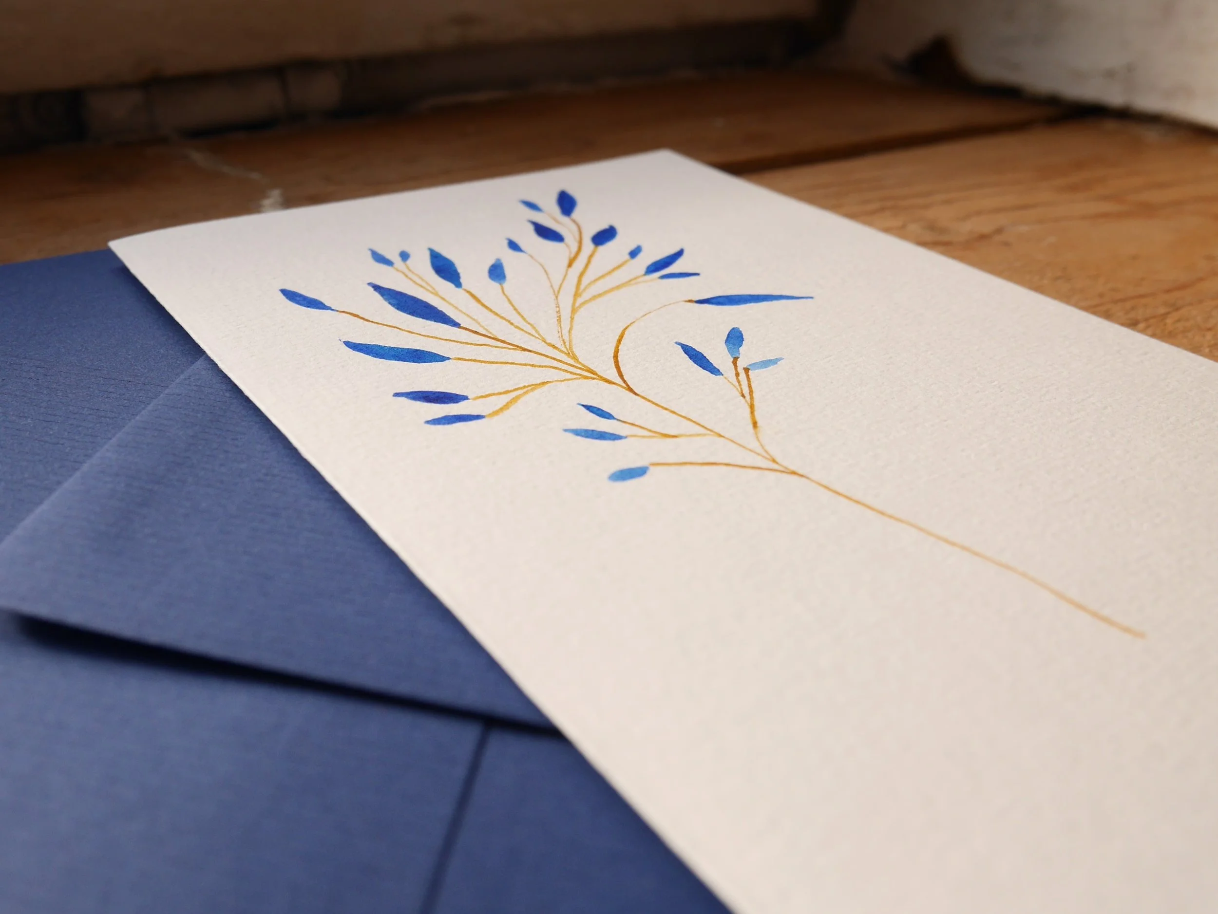 Klappkarte mit gemaltem Zweig mit blauen Blättern und blauem Umschlag