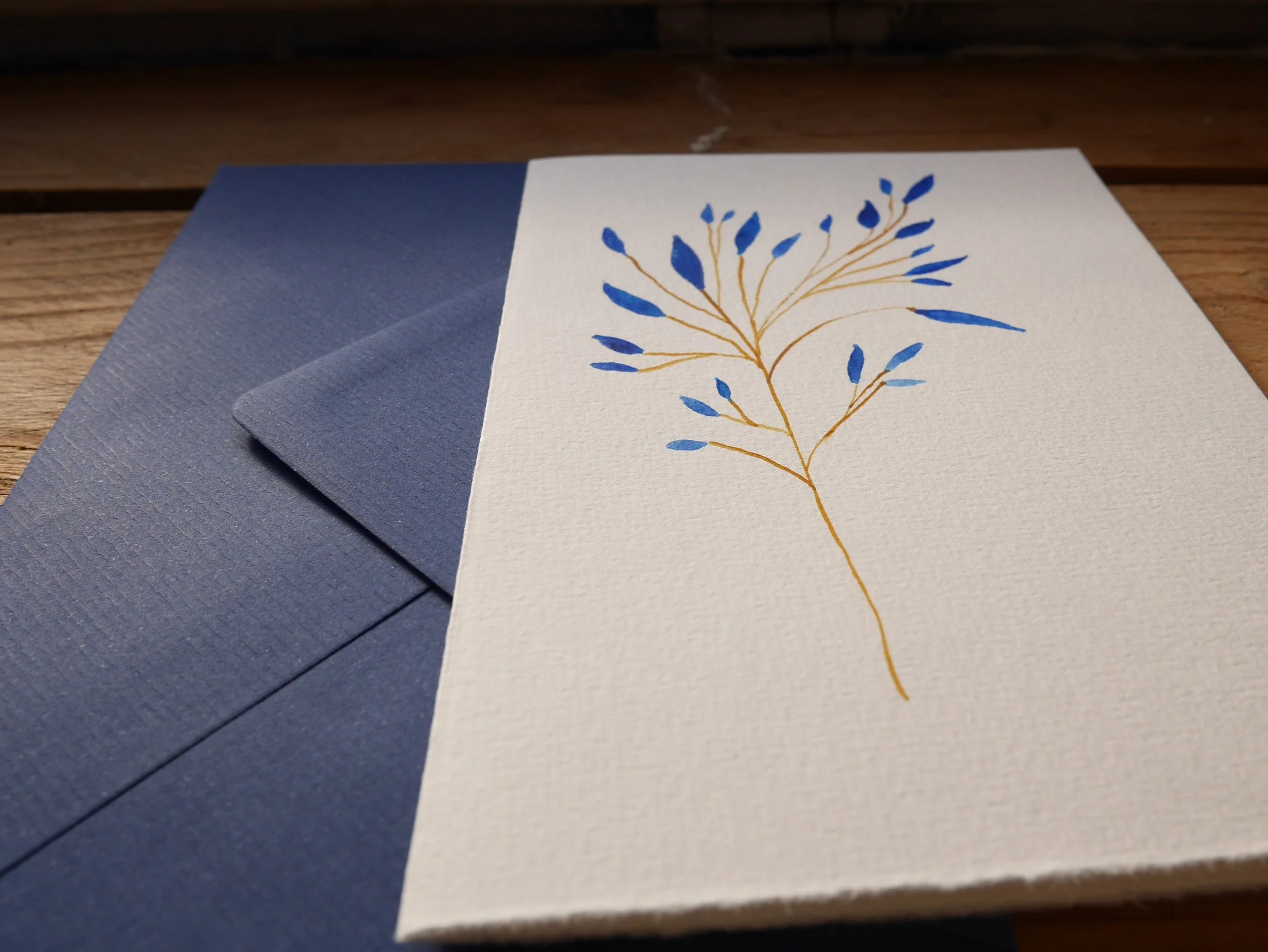 Klappkarte mit gemaltem Zweig mit blauen Blättern und blauem Umschlag