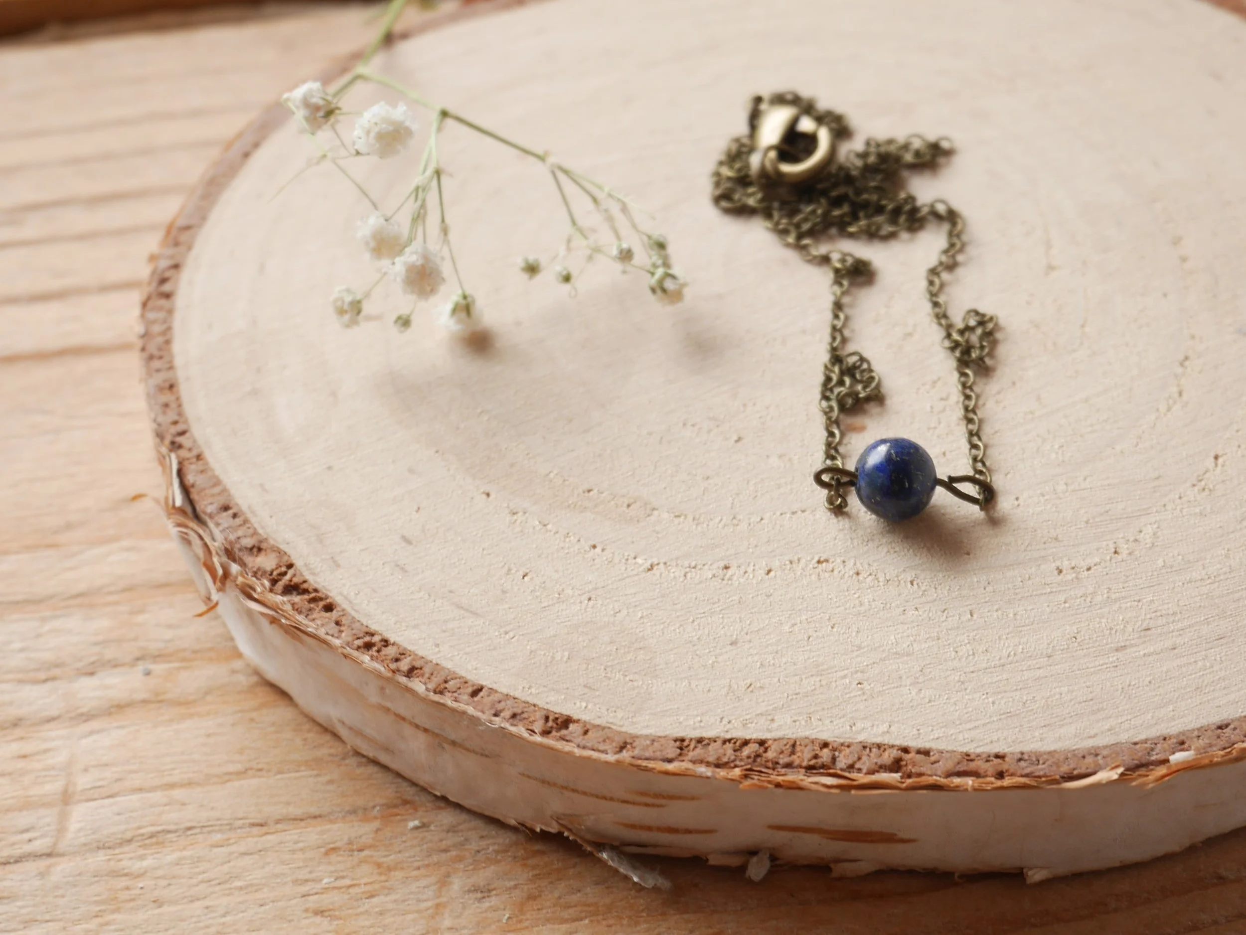 eine bronzefarbene Halskette mit einer kleinen blauen Perle liegt neben einer getrockneten Blüte