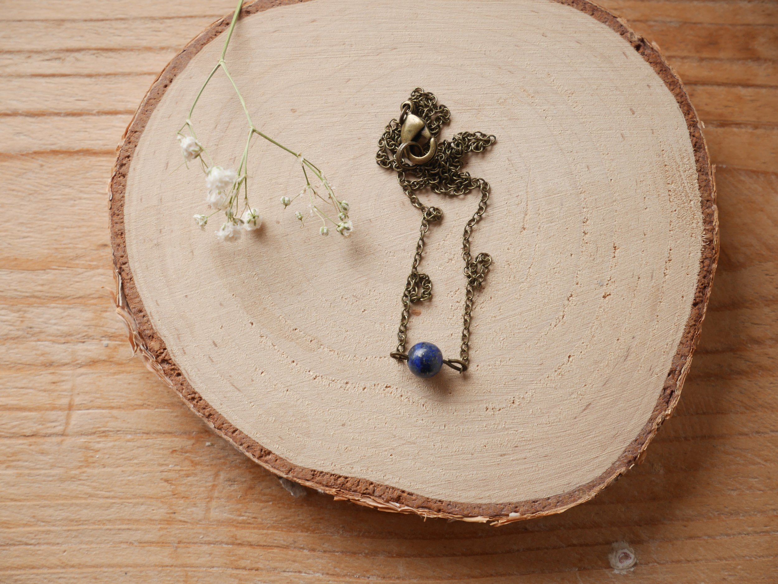 eine bronzefarbene Halskette mit einer kleinen blauen Perle liegt neben einer getrockneten Blüte