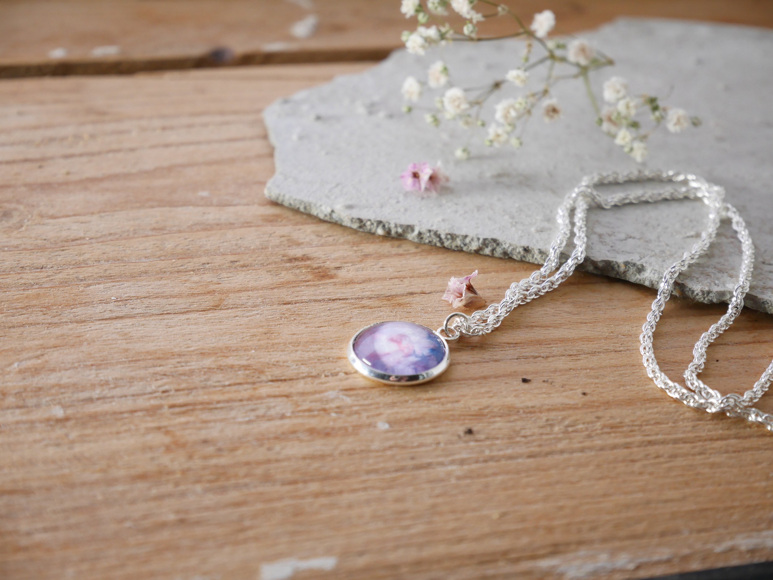 Silberne, gedrehte Halskette mit einem runden Anhänger, darin ein rosa-blau bemalter Glasstein