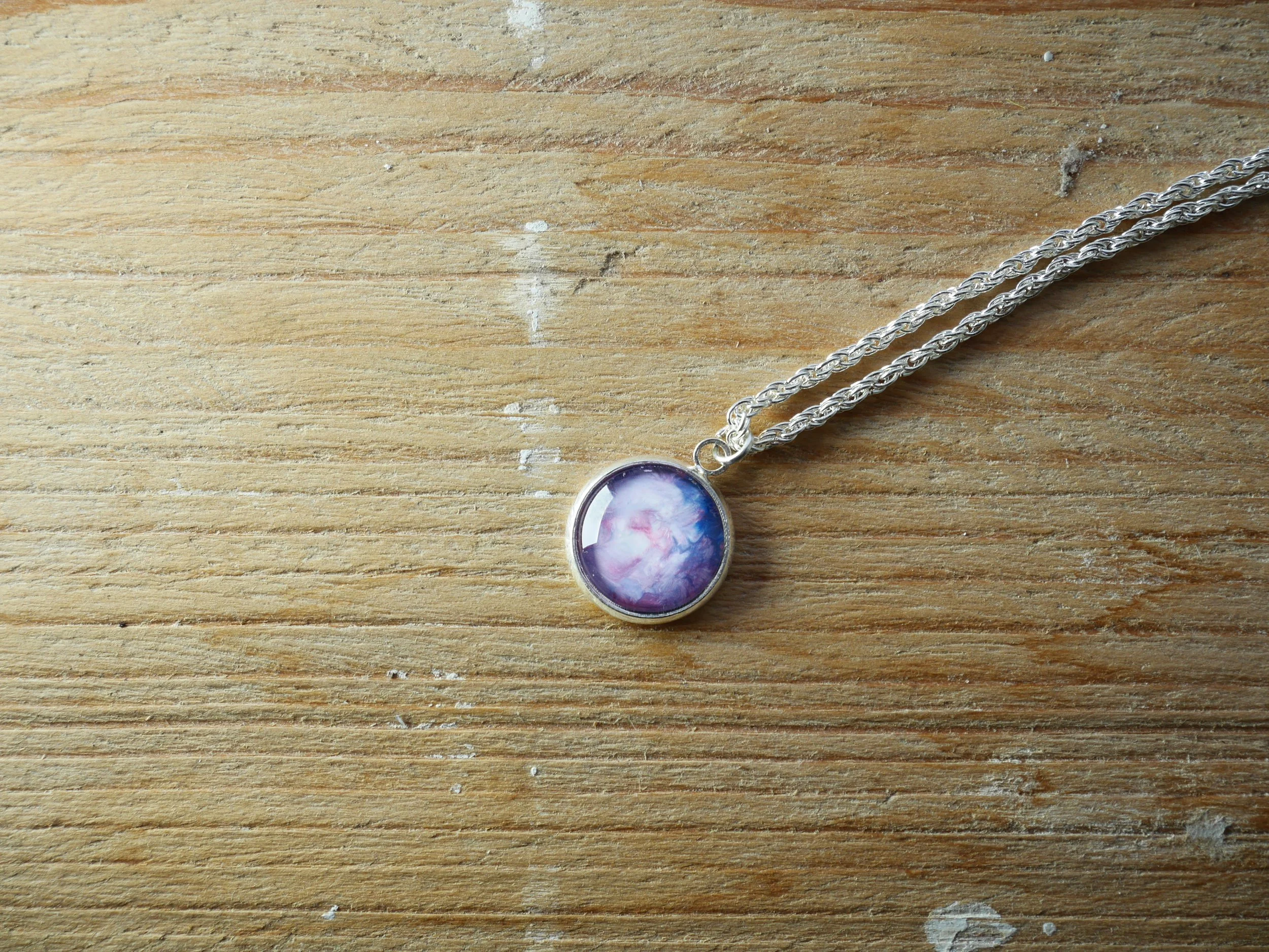 Silberne, gedrehte Halskette mit einem runden Anhänger, darin ein rosa-blau bemalter Glasstein
