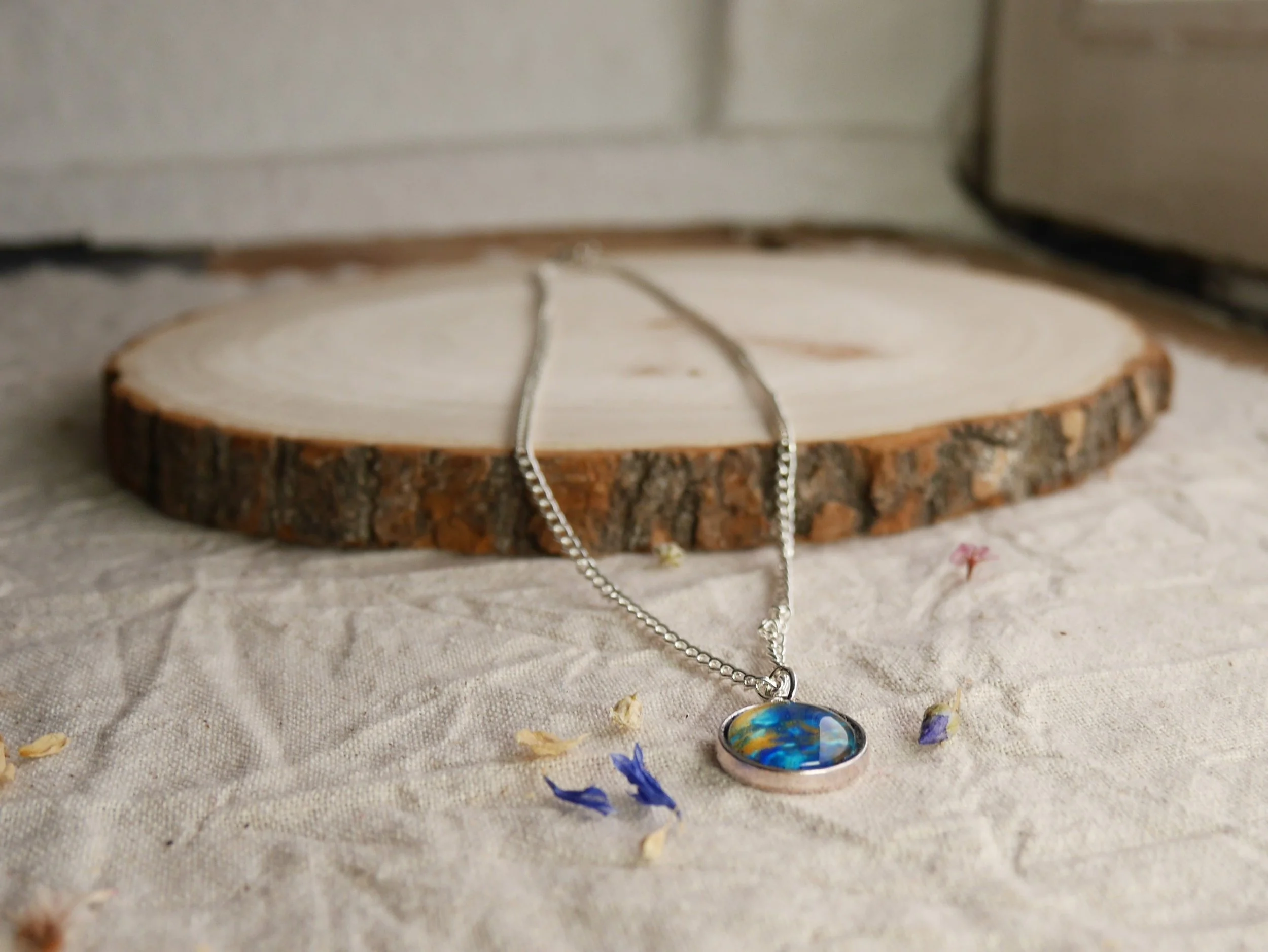 Silberne Halskette mit rundem Anhänger, darin eingefasst ein halbrunder Glasstein in blau, gold und glitzernd